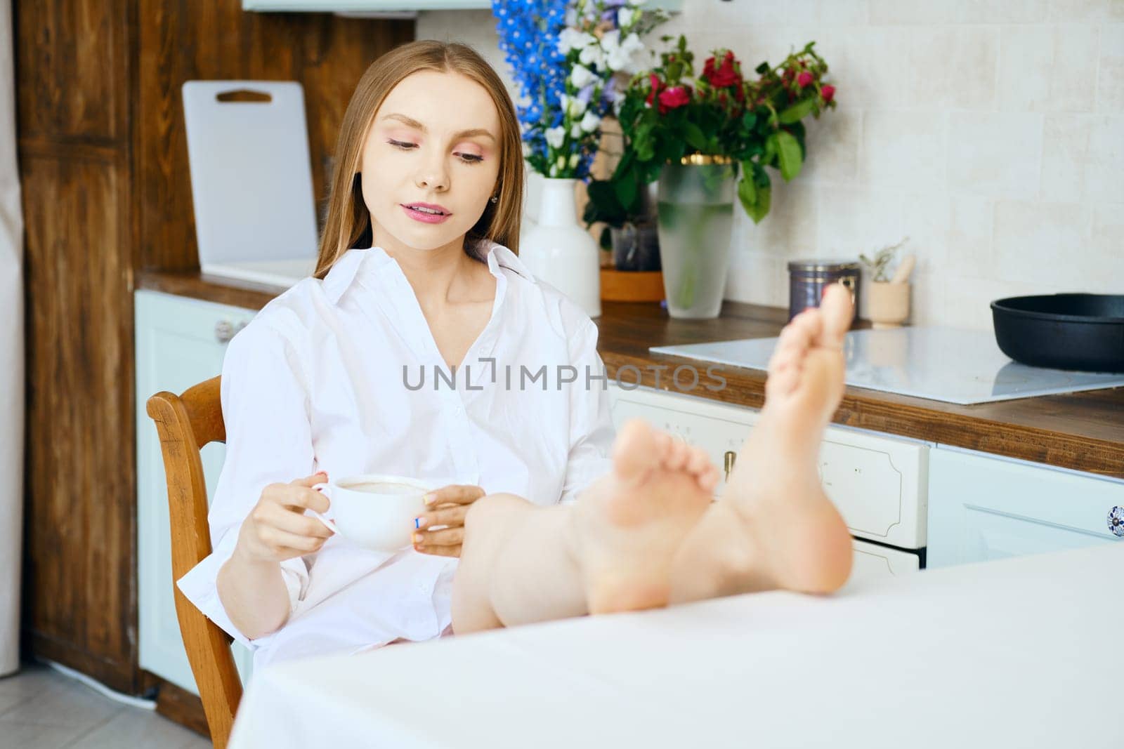 Young woman sitting at table in kitchen with cup of coffee