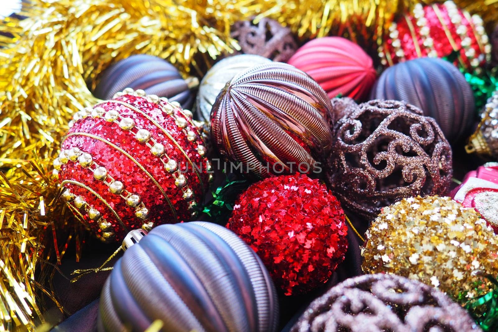 Christmas background with yellow tinsel and Christmas balls. Beautiful Christmas toys and decorations. Red, gold, brown, silver, yellow striped shiny balls. Toy festive train locomotive
