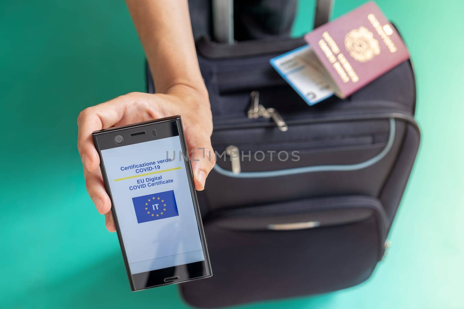 Woman showing on smartphone Italian EU Digital Covid Certificate with quad code. Passport, boarding pass and baggage.