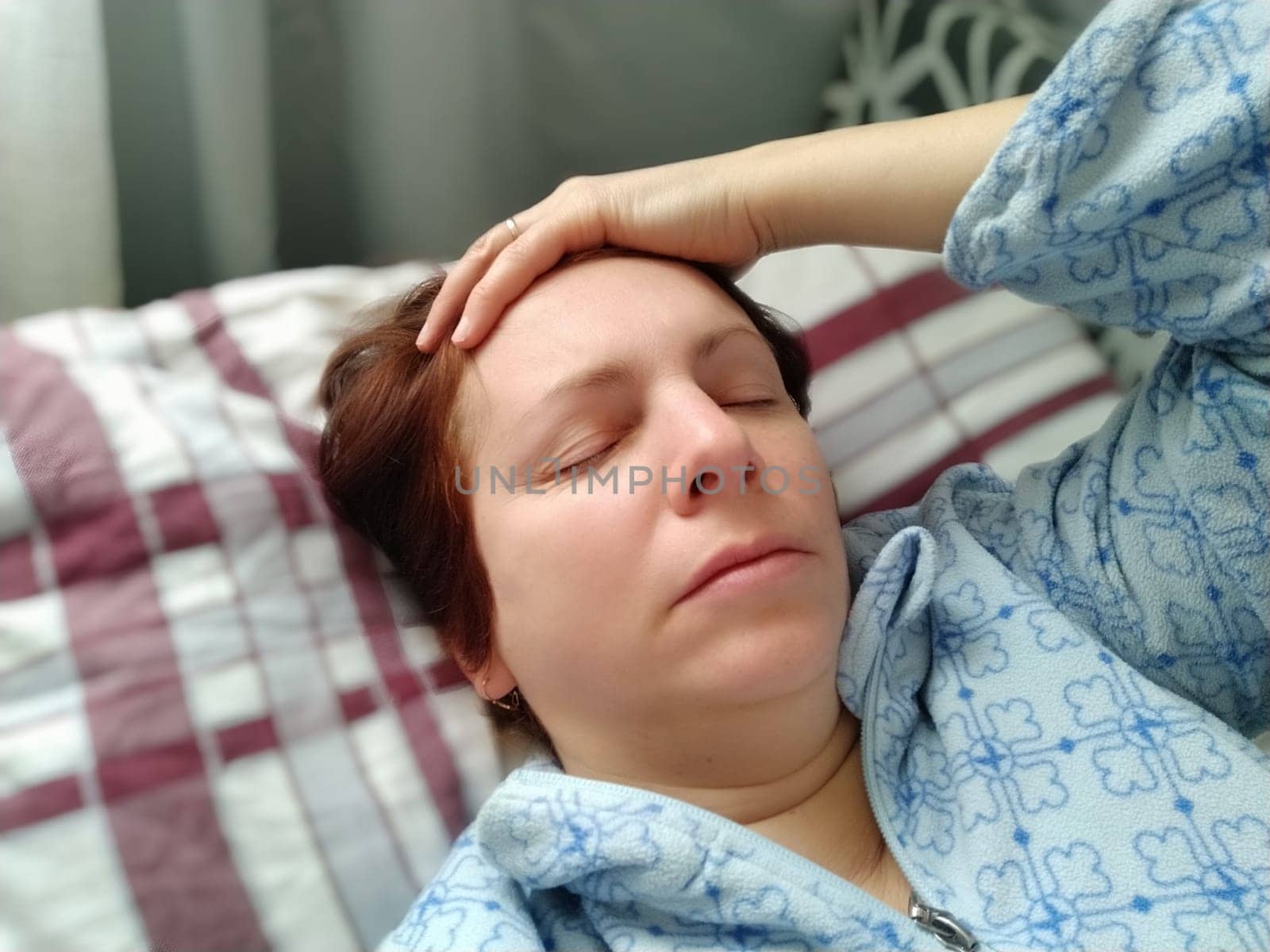 Sick woman in bed. Headache, runny nose and cold. Paleness of the face and faintness of the body. Feeling unwell. The patient holds his forehead with his hand and covers his eyes.