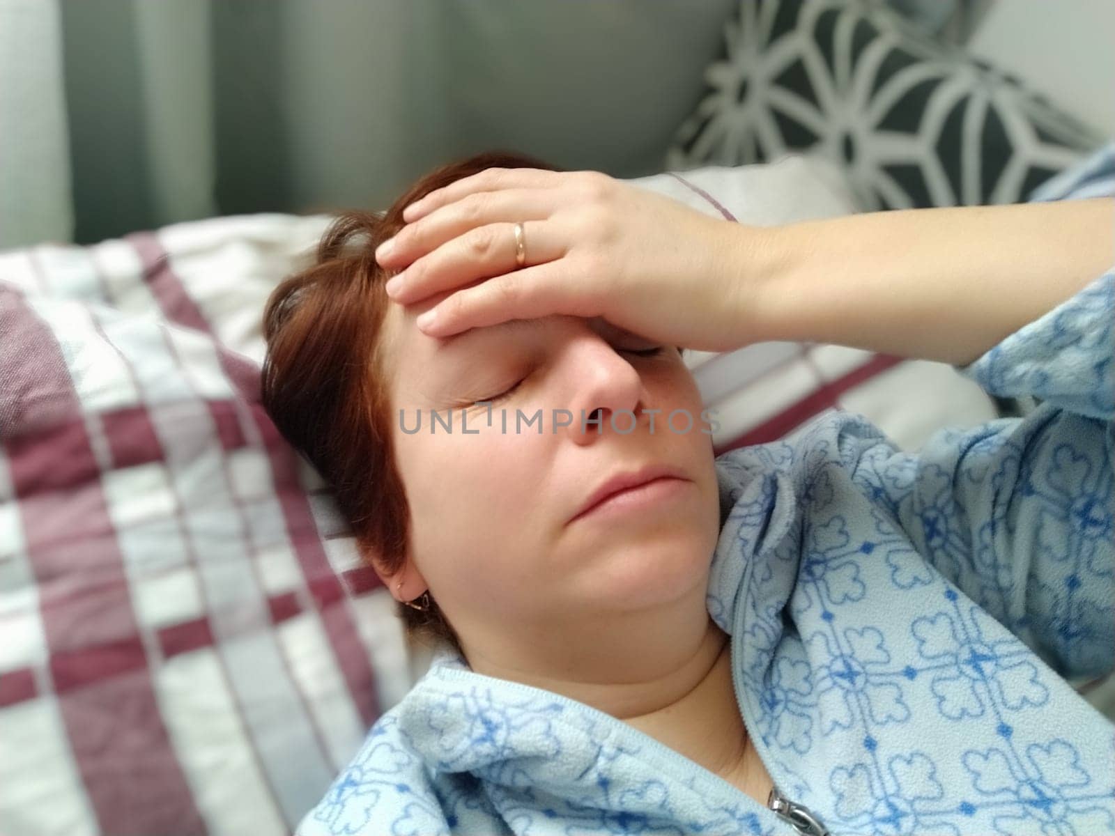 Sick woman in bed. Headache, runny nose and cold. Paleness of the face and faintness of the body. Feeling unwell. The patient holds his forehead with his hand and covers his eyes.