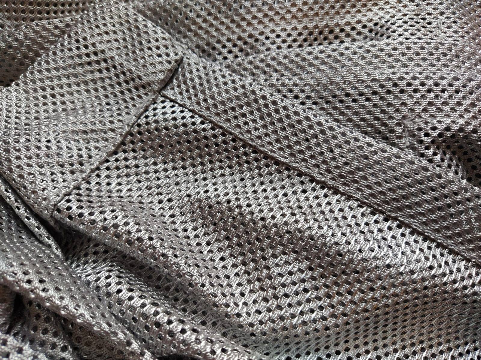 Synthetic polyester fabric with holes. Abstract background. A wave-folded piece of fabric in gray or silver color. Neatly hemmed fabric
