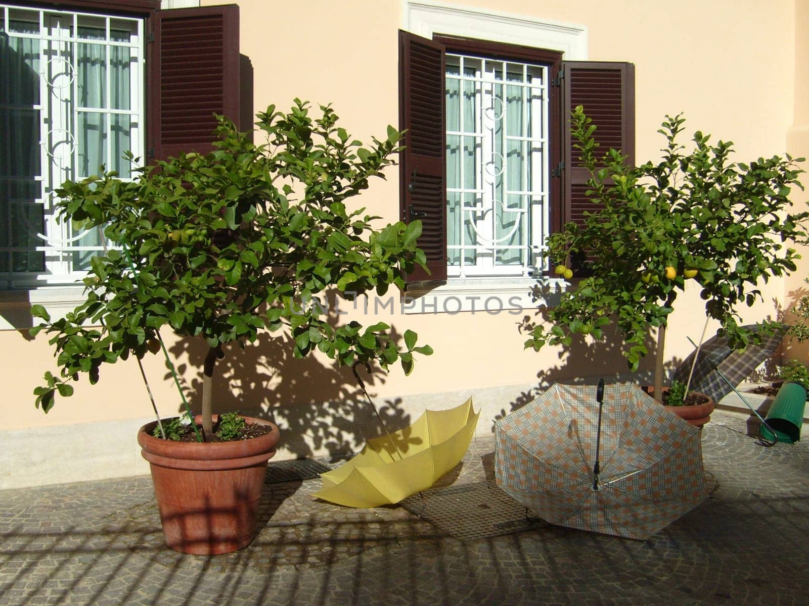 Umbrellas at the wall of an Italian house. Wooden shutters are open on the windows with white curtains. Tourism, recreation and weather theme. Changeable weather.