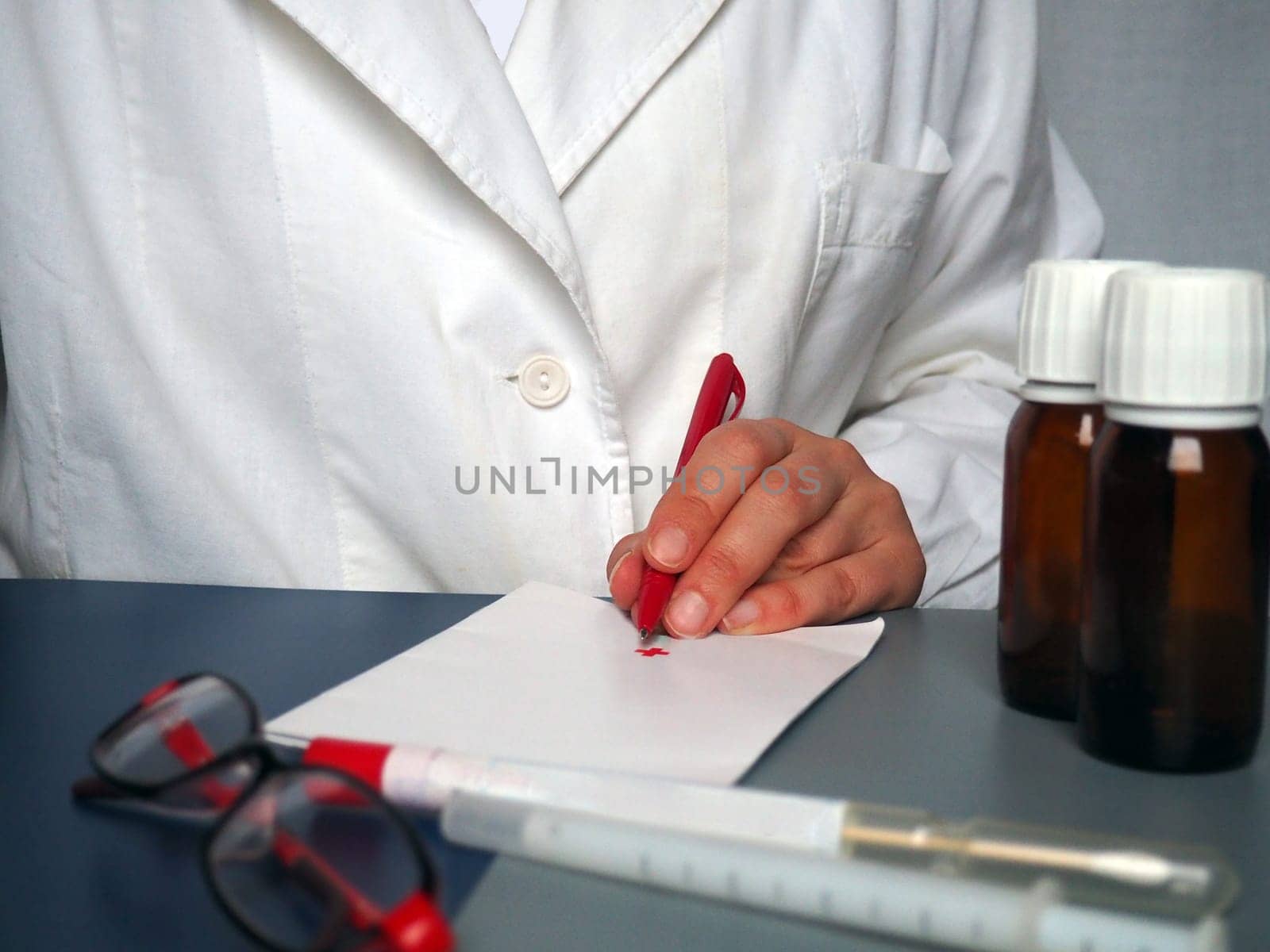 A left-handed doctor is writing something down on paper. Pen for writing in hand. A white coat is worn by a medical professional. Hands of a doctor or nurse. Medicines, glasses, test tubes