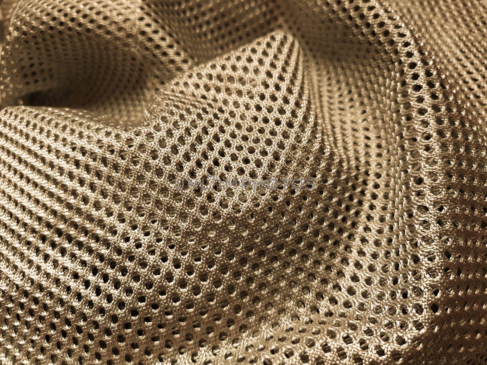 Synthetic polyester fabric with holes. Abstract background. A piece of fabric, folded in waves, in yellow or gold. Furniture upholstery.