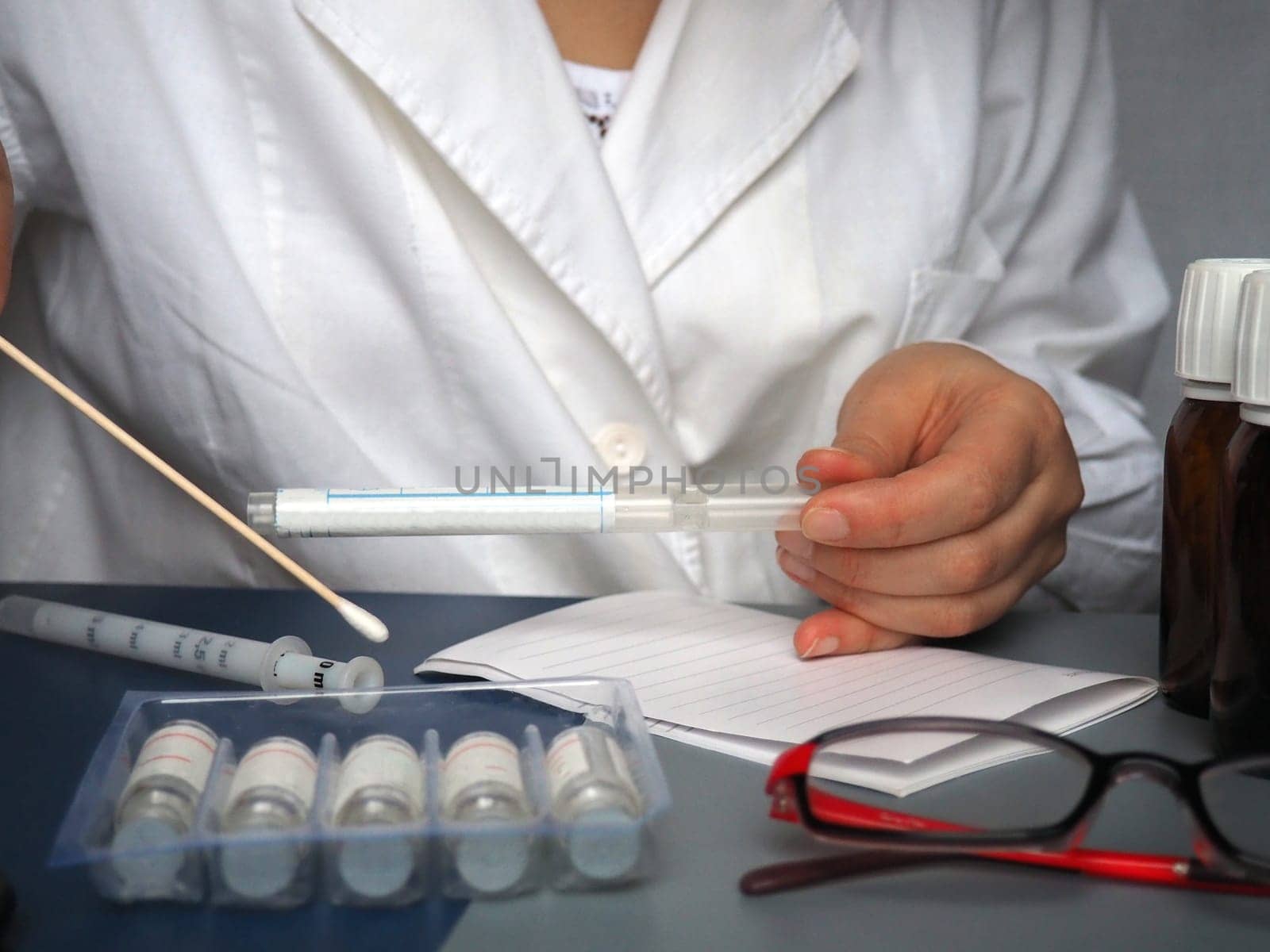Hands of a doctor or nurse. Virus and bacteria test in hand. A white coat is worn by a medical professional. Medicines, glasses, test tube and a syringe are on the table. Medic at work on diagnostics