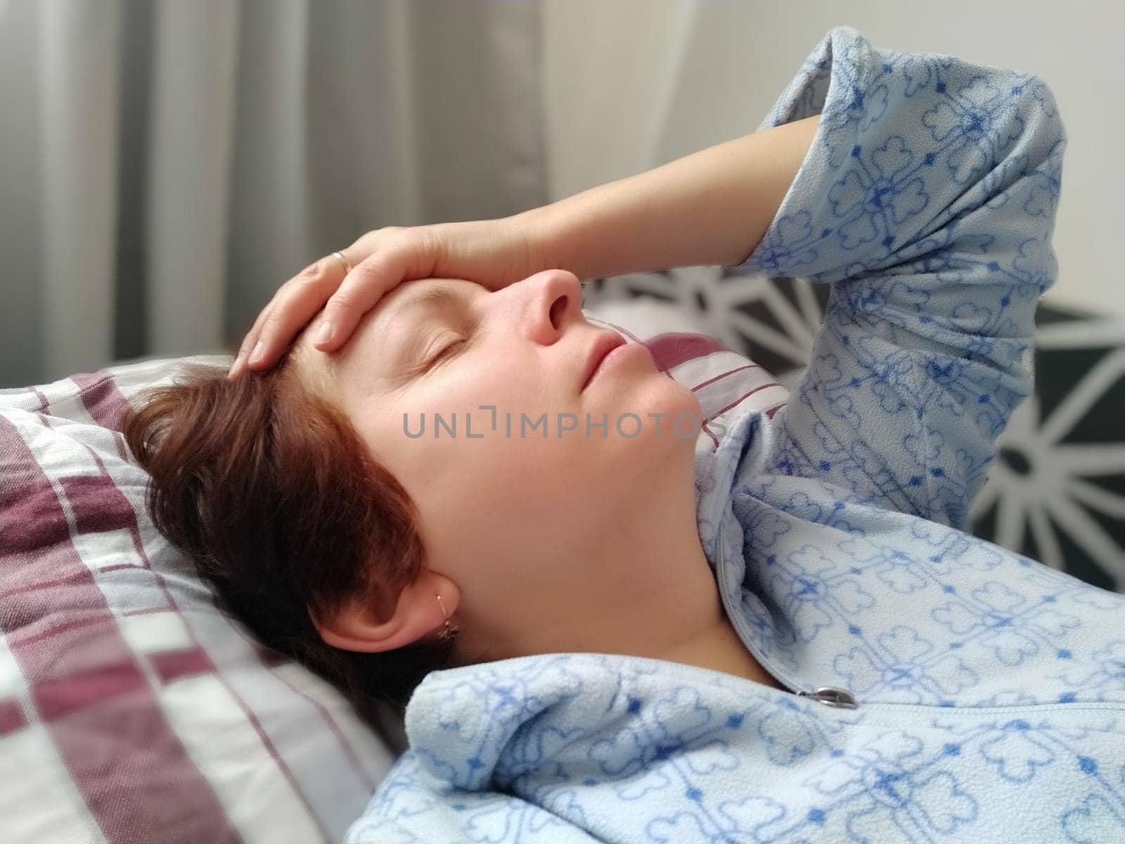 Sick woman in bed. Headache, runny nose and cold. Paleness of the face and faintness of the body. Feeling unwell. The patient holds his forehead with his hand and covers his eyes.