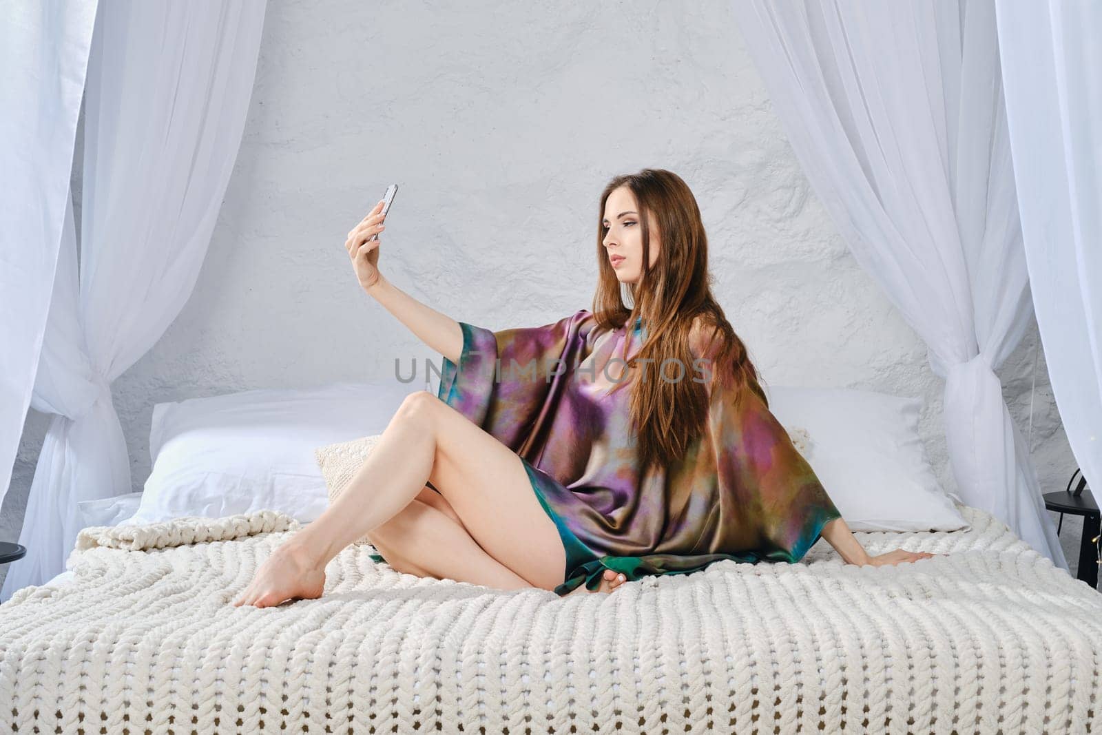 Calm satisfied woman relaxing on comfortable bed enjoying weekend at home and making online video call