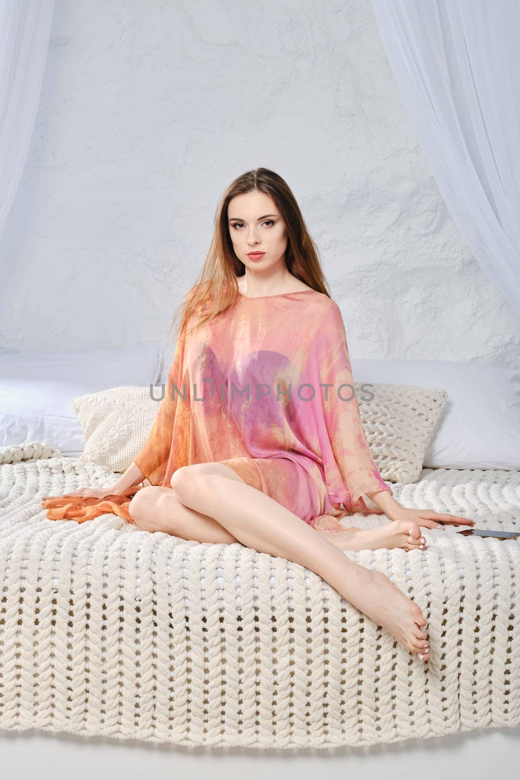 Calm young woman in silk robe sitting on bed. The concept of comfort, coziness and relaxation at home.