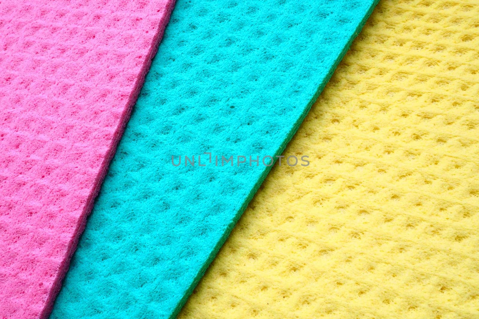 A set of cleaning wipes, microfiber cloths or sponges for the kitchen, three multi-colored cloths. Sponge fibers sponge texture pattern surface close-up background. Pink, blue and yellow