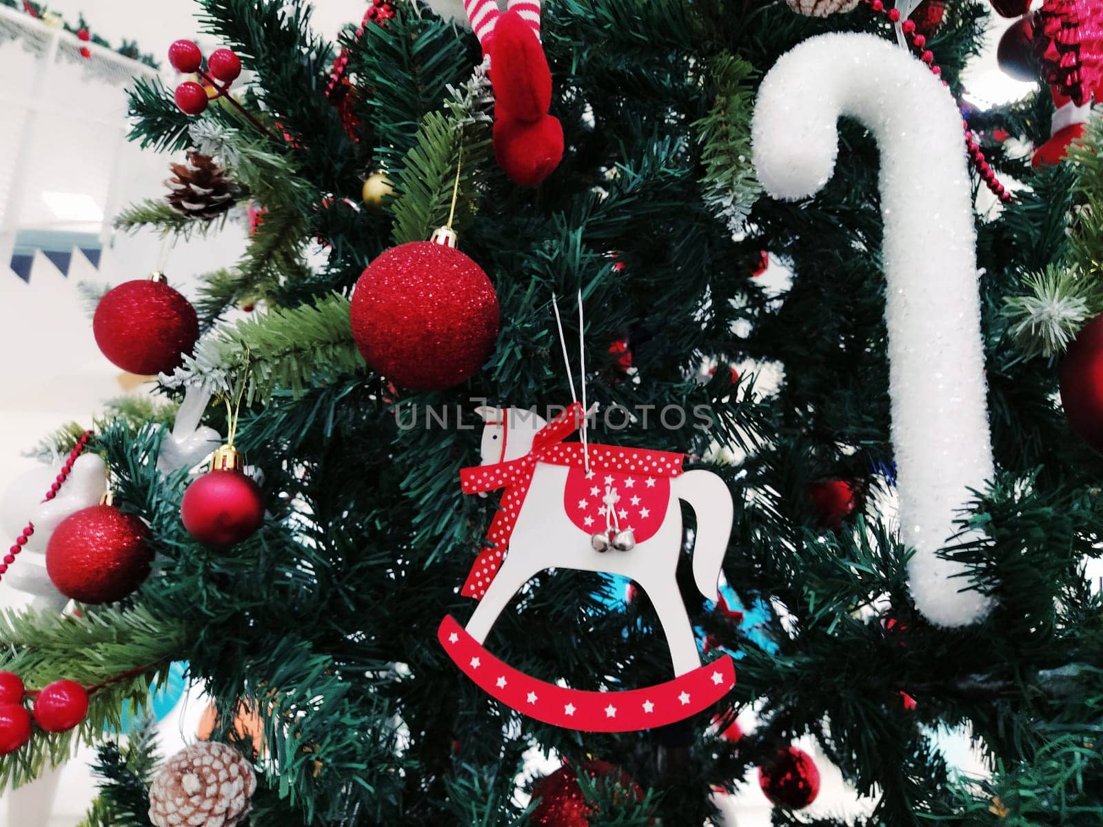 Christmas tree with decorations, Christmas balls and toys. Red and white hanging ornaments. Beautiful balls, bright berries and cones. Snow candy stick. Toy - rocking horse.