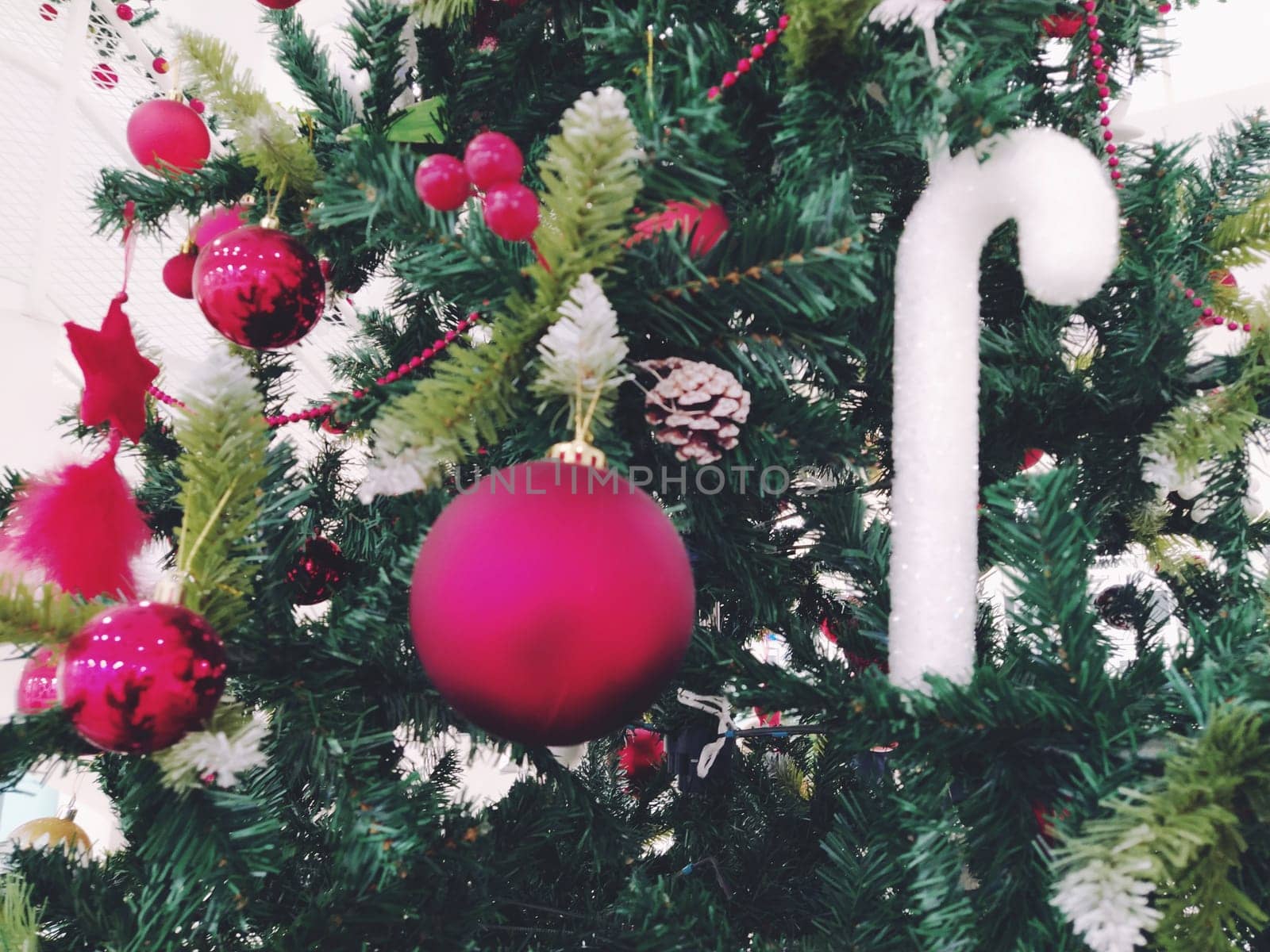 Christmas tree with decorations, Christmas balls and toys. Red and white hanging ornaments. Beautiful balls, bright berries and cones. Snow candy stick.