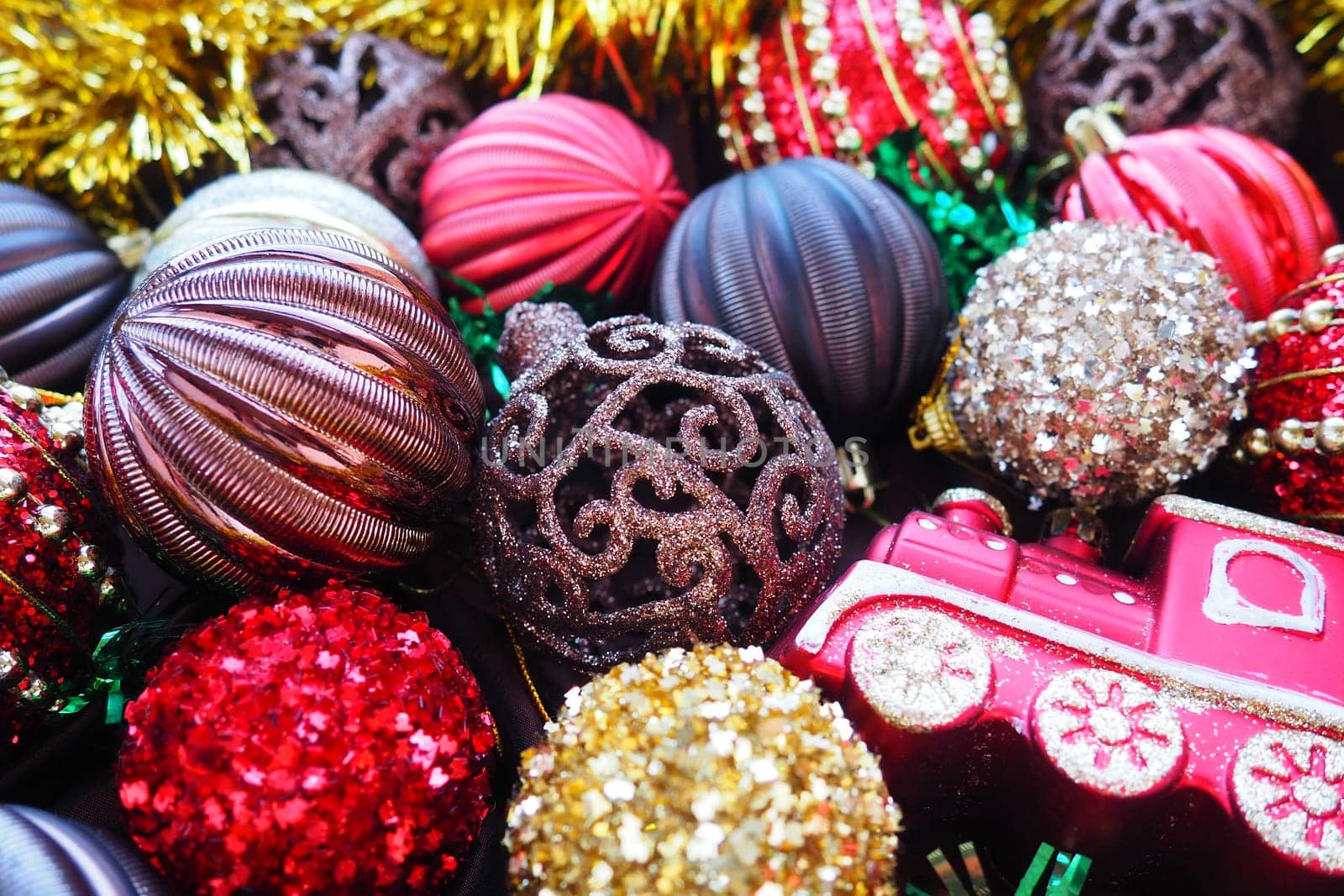 Christmas background with yellow tinsel and Christmas balls. Beautiful Christmas toys and decorations. Red, gold, brown, silver, yellow striped shiny balls. Toy festive train locomotive