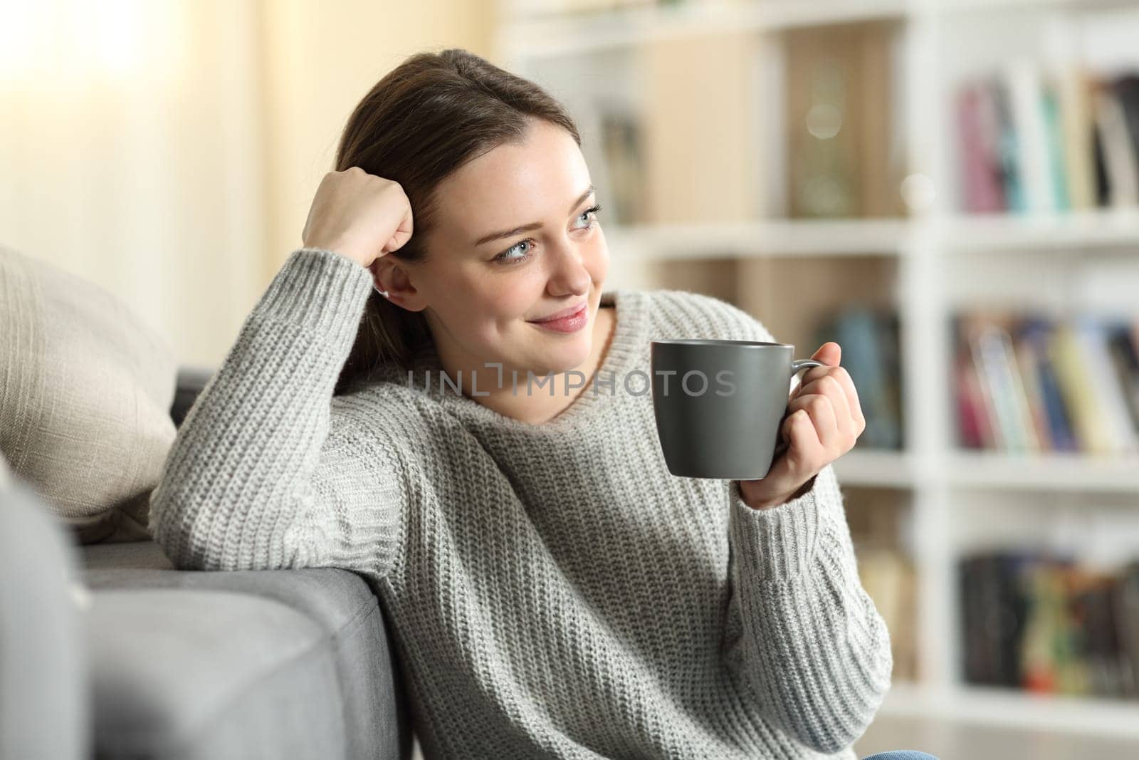 Happy teen holding coffee cup dreaming sitting at home