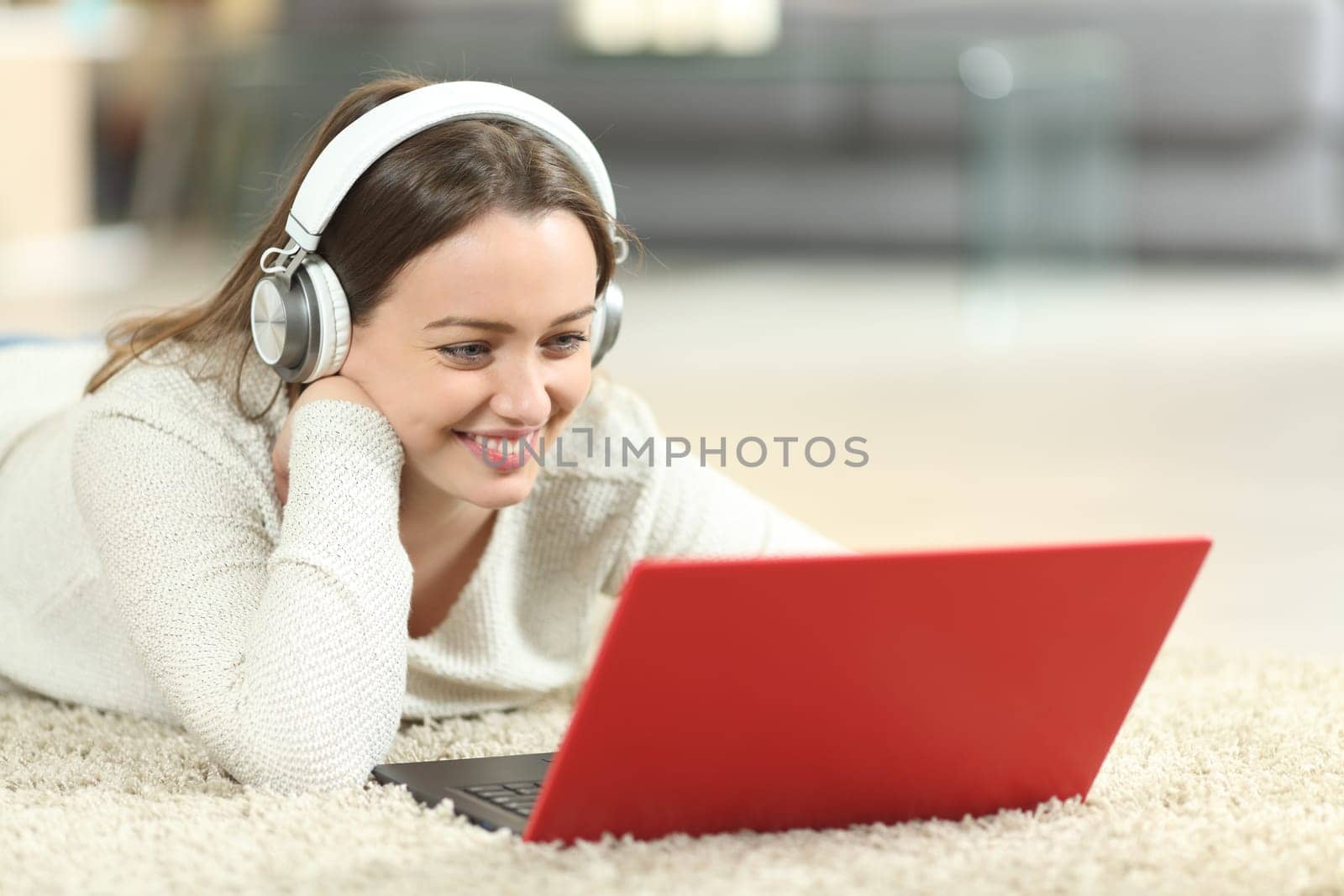 Happy teen wearing headphones watching media on laptop on the floor at home