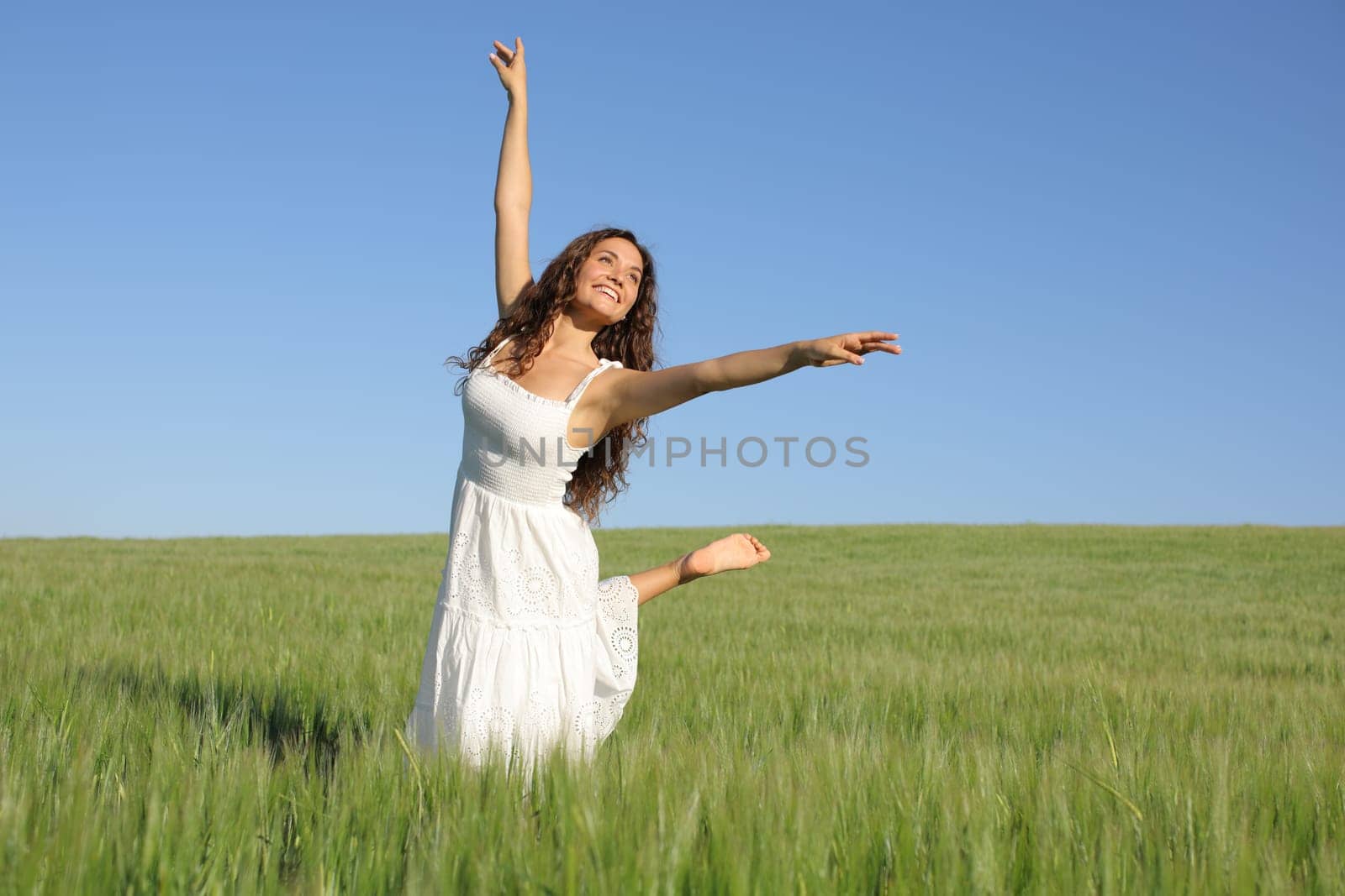 Happy woman with white dress dancing in a green wheat field