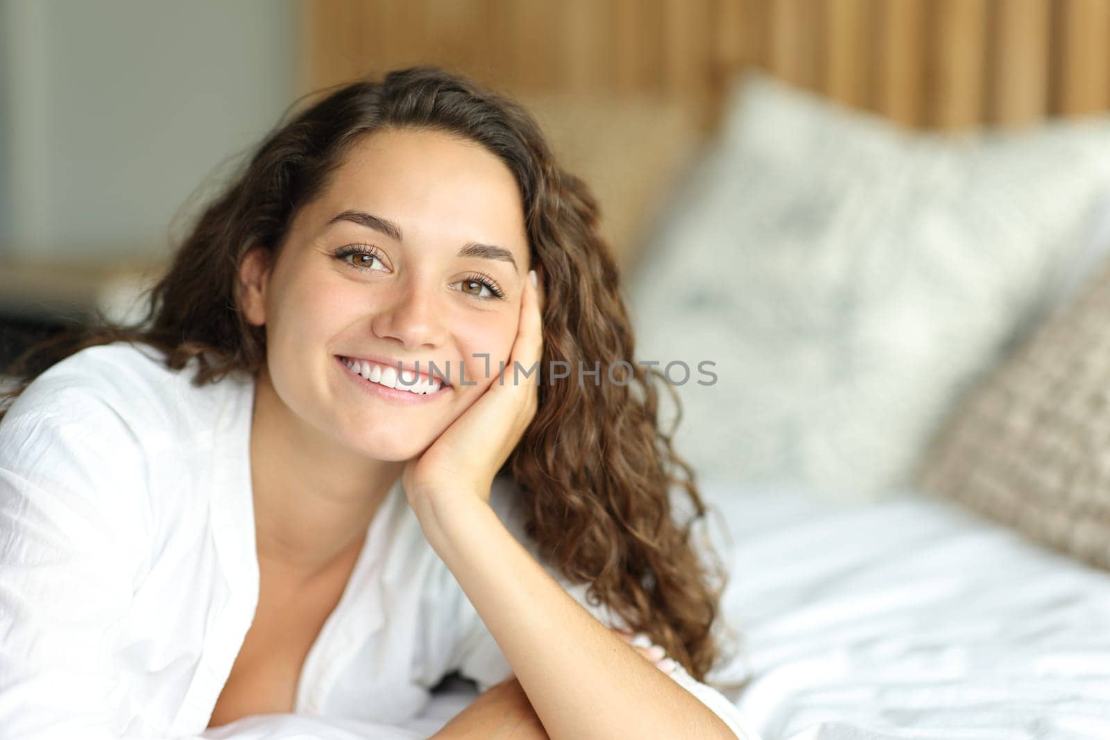 Portrait of a happy woman looking at camera on a bed smiling in the bedroom