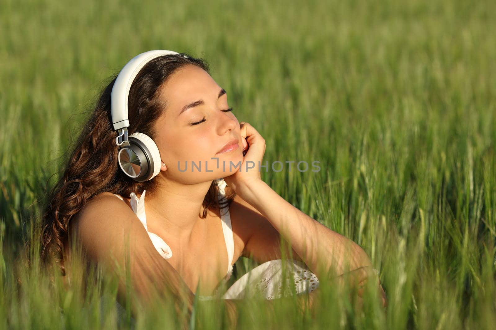 Woman relaxing listening to music wearing headphones in a green barley field