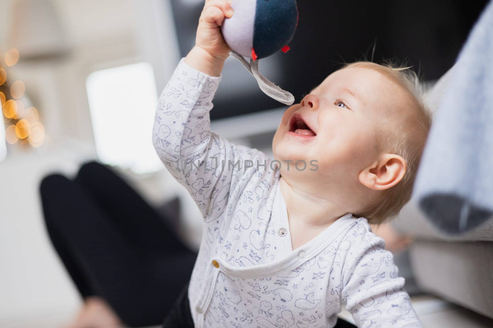 Cute infant baby boy playing, crawling and standing up by living room sofa at home. Baby playing at home
