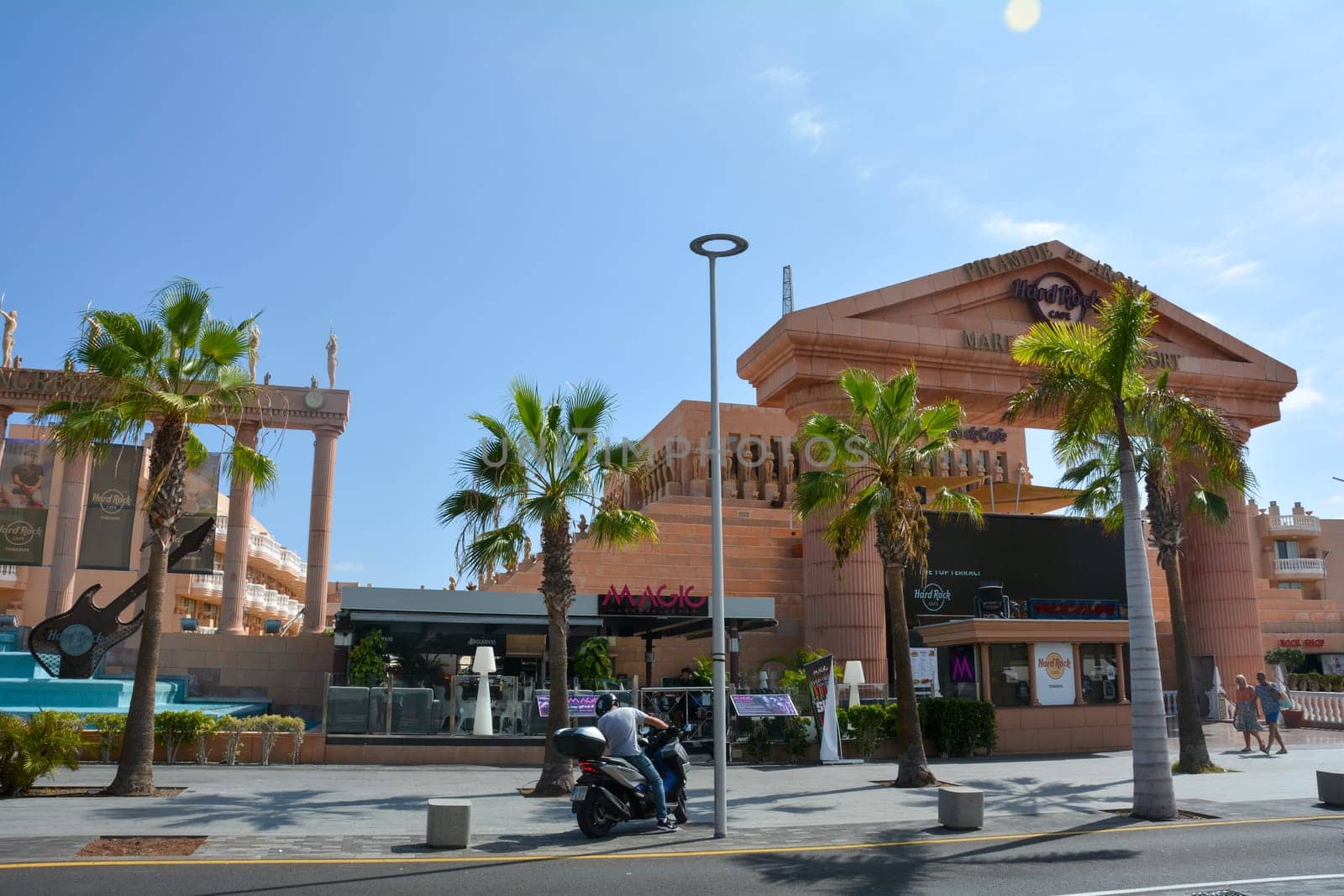 Hard Rock Cafe, Playa de la Americas, Tenerife, Spain August 12, 2022 - View from across the street of the Cafe building with a motorbike and palm trees and blue sky