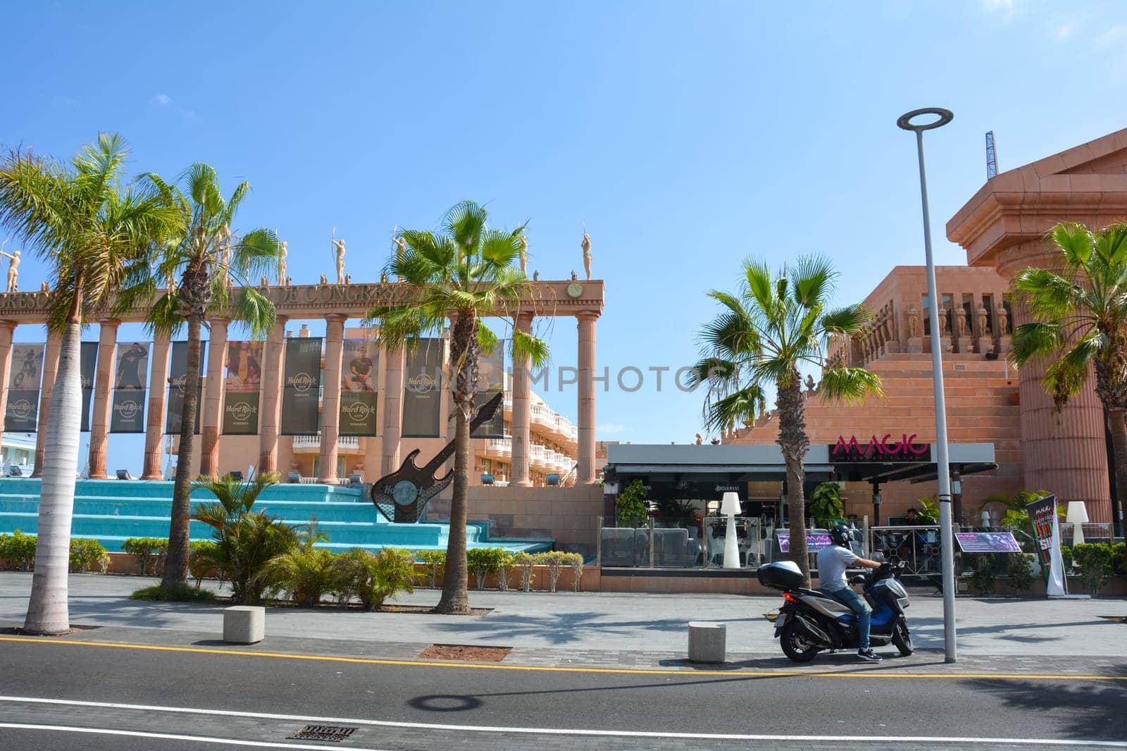 Hard Rock Cafe, Playa de la Americas, Tenerife, Spain August 12, 2022 - View from across the street of the Cafe building with a motorbike and palm trees and blue sky