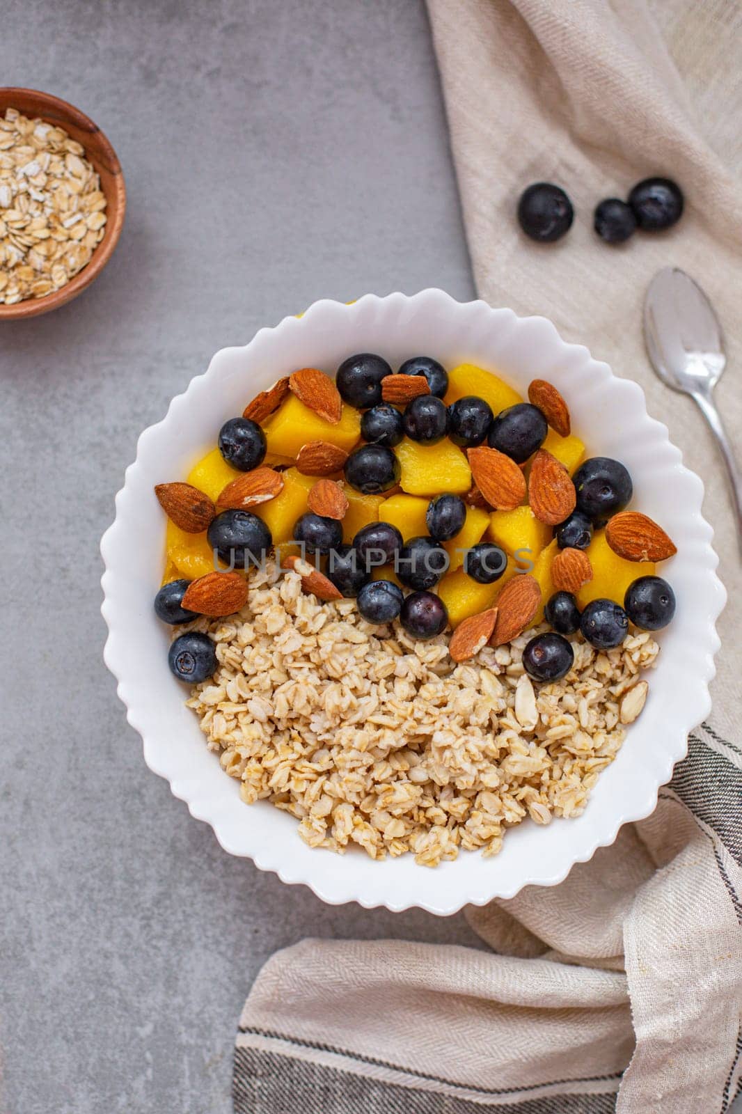 Oatmeal porridge with blueberries, mango and almonds in bowl on concrete grey table from above. flatlay. Healthy breakfast food. Copy space