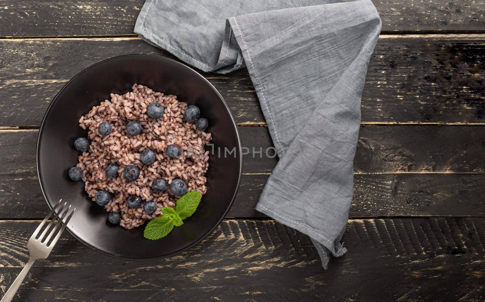 Italian risotto with blueberries with cheese and fresh green mint leaves on black wooden table. Flatlay, Copy space for text.