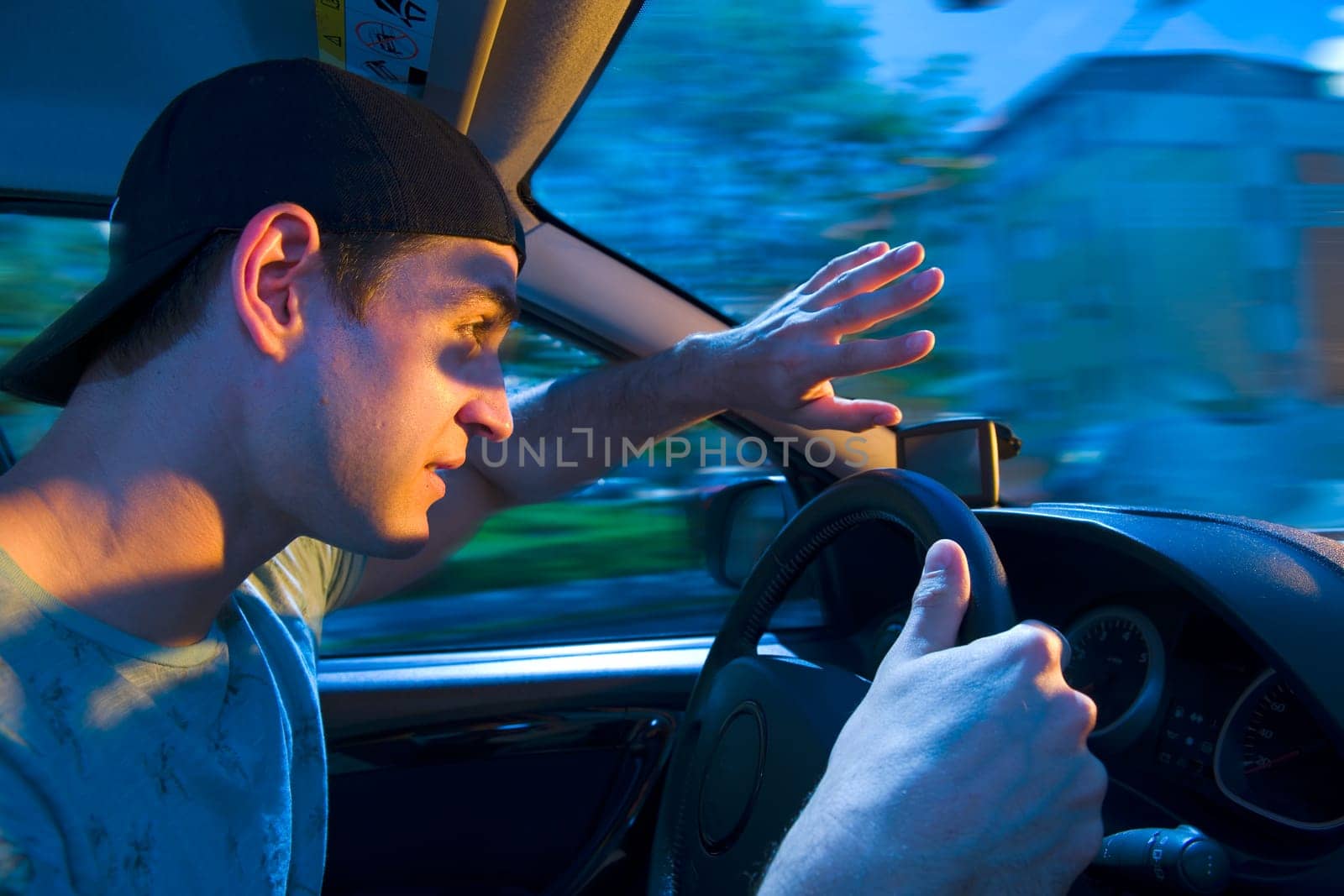 Side wide-angle upper body interior view of a blinded motorist (young man) holding his hands protectively in front of him towards the windshield with shocked look