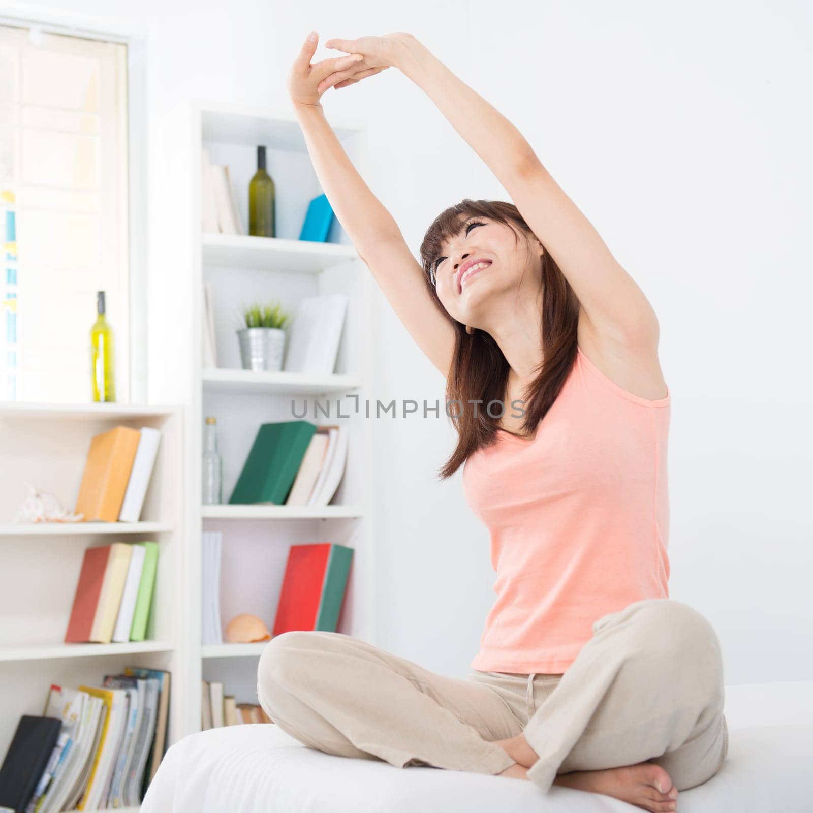 Portrait of awake Asian girl stretching arms in the morning. Young woman indoors living lifestyle at home.