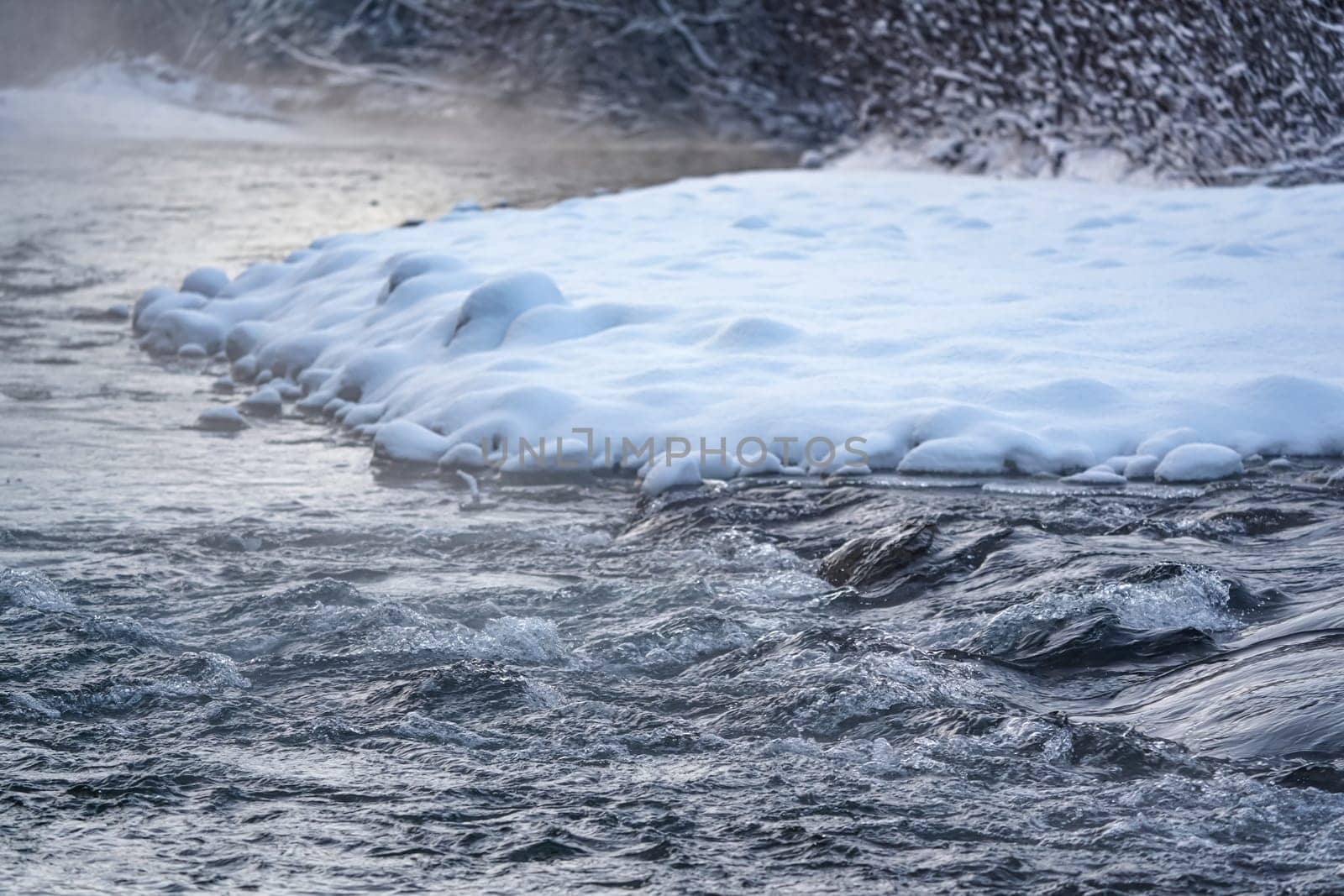 Cold winter river, steam visible above water, dark trees on side.