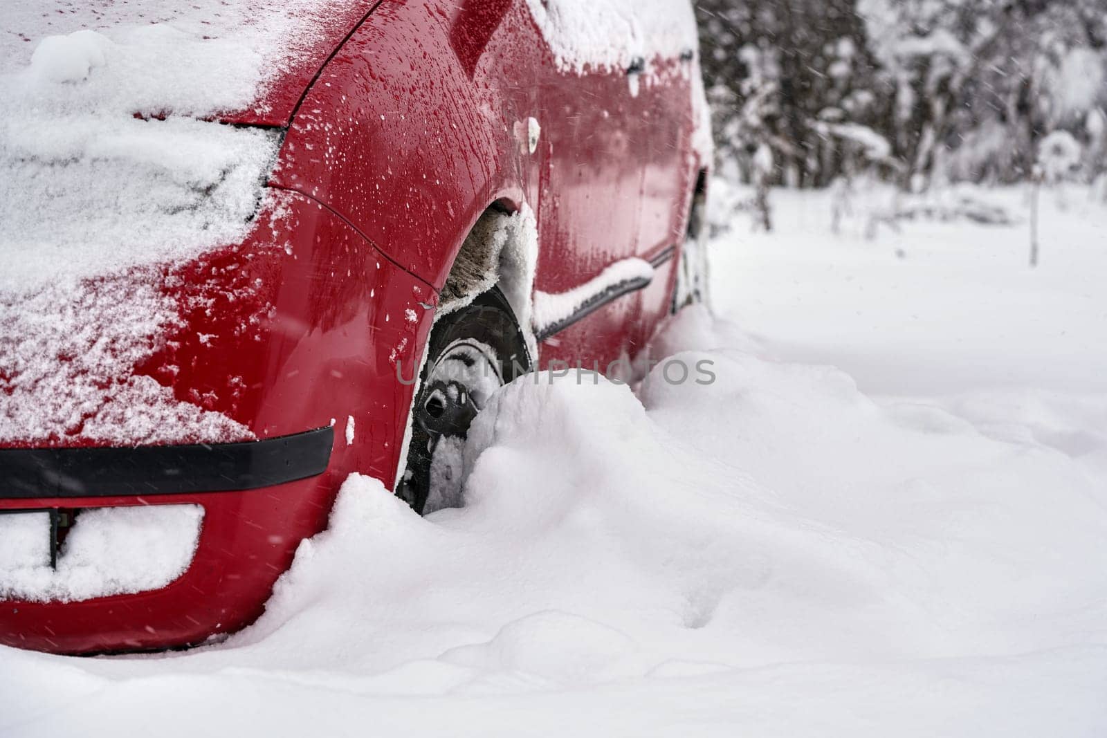 Red car parked in deep layer of snow after heavy snowstorm, detail to tire - only half wheel visible.