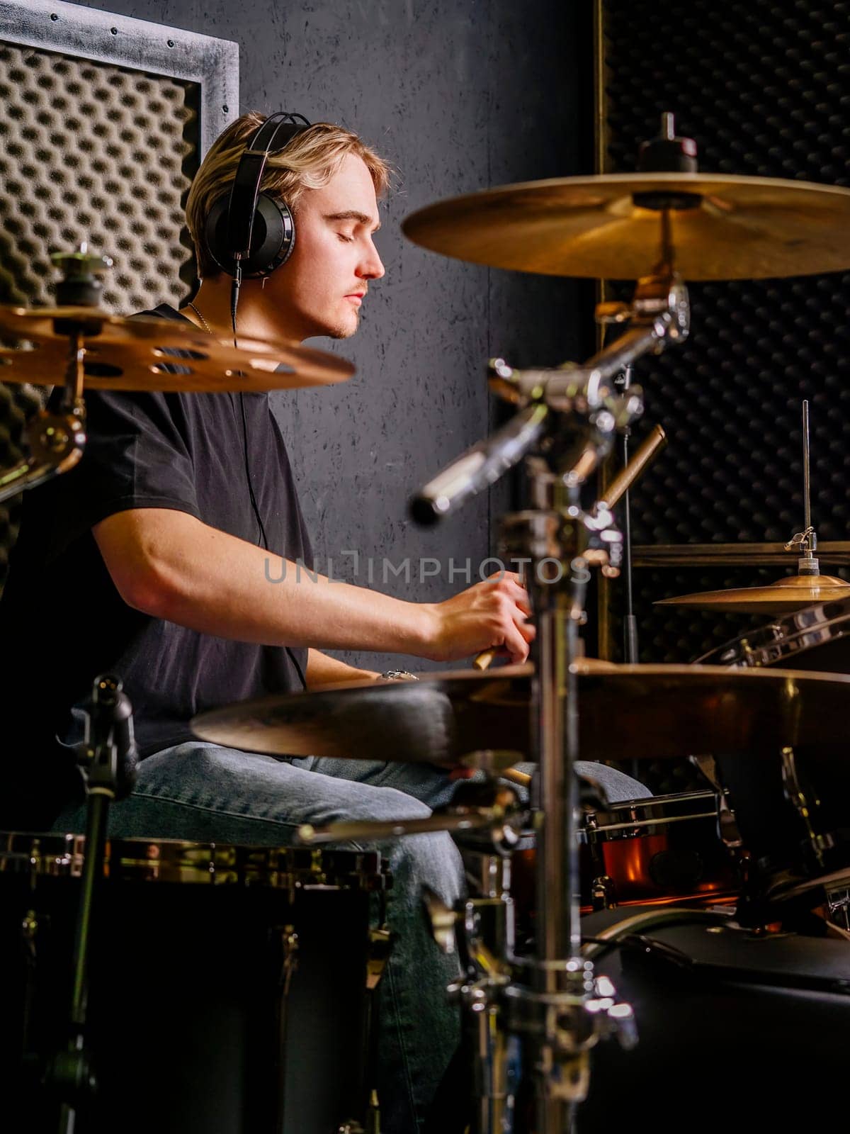 Young man wearing headphones and playing drums in a recording studio.