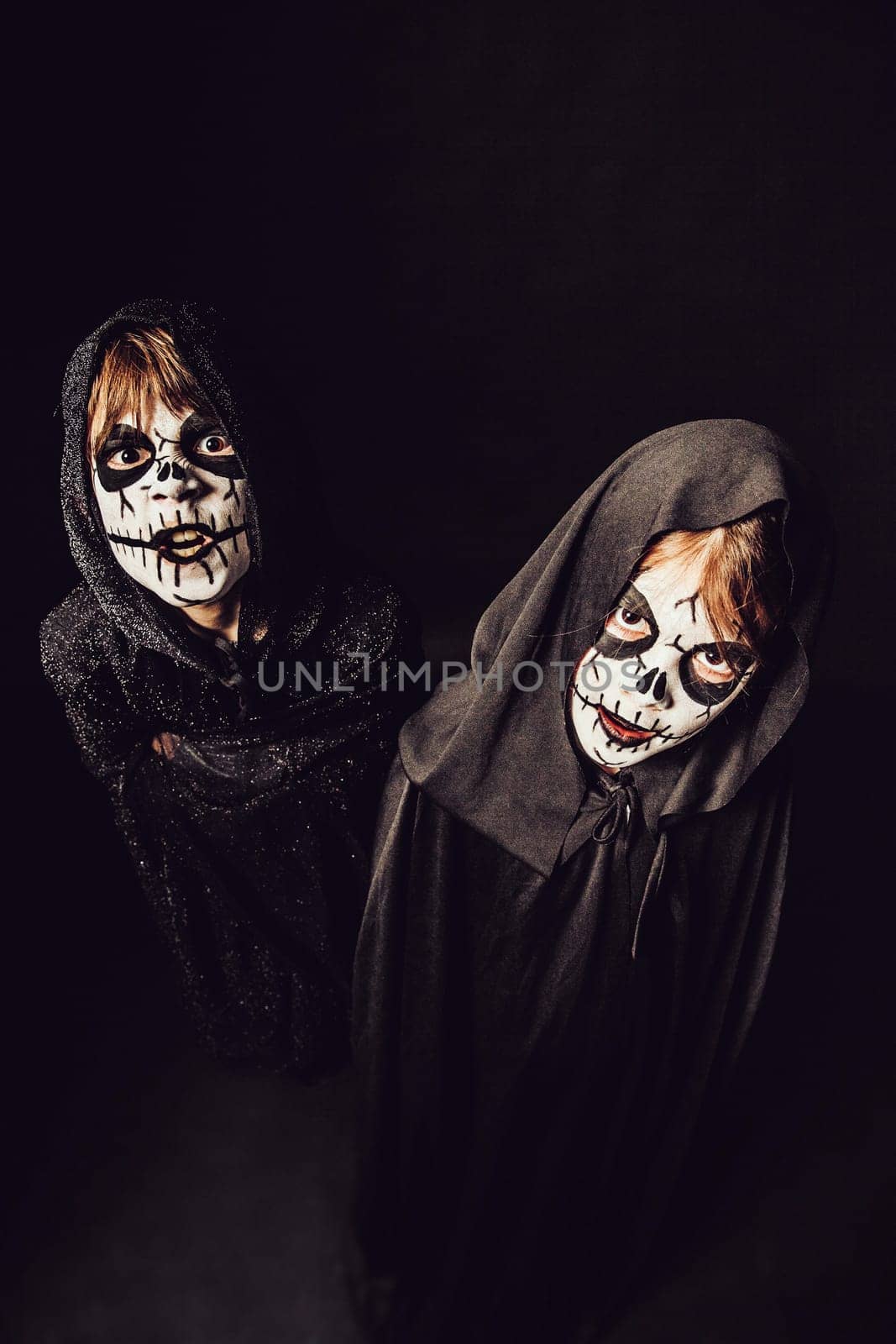 Two kids wearing dark robes and scary face paint at Halloween.