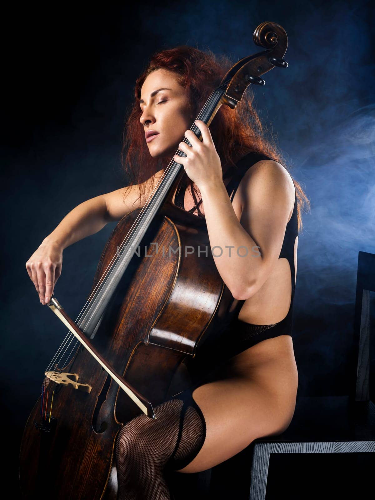 Photo of a beautiful woman in lingerie concentrating on her cello playing.