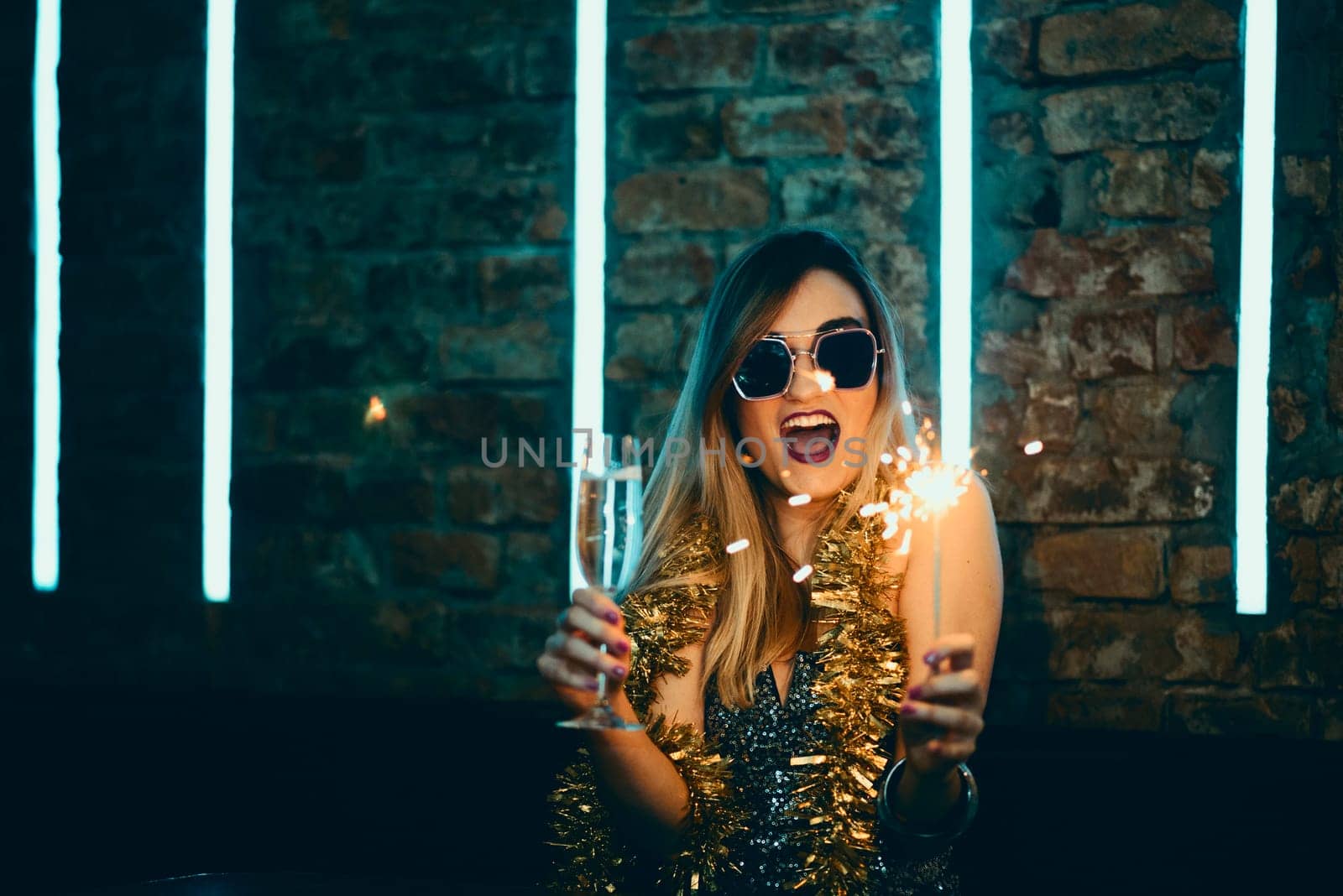 Young happy woman celebrating new year eve drinking champagne with fireworks and confetti. Lady clubber in nightclub having fun. Hipster girl at celebration luxury party.
