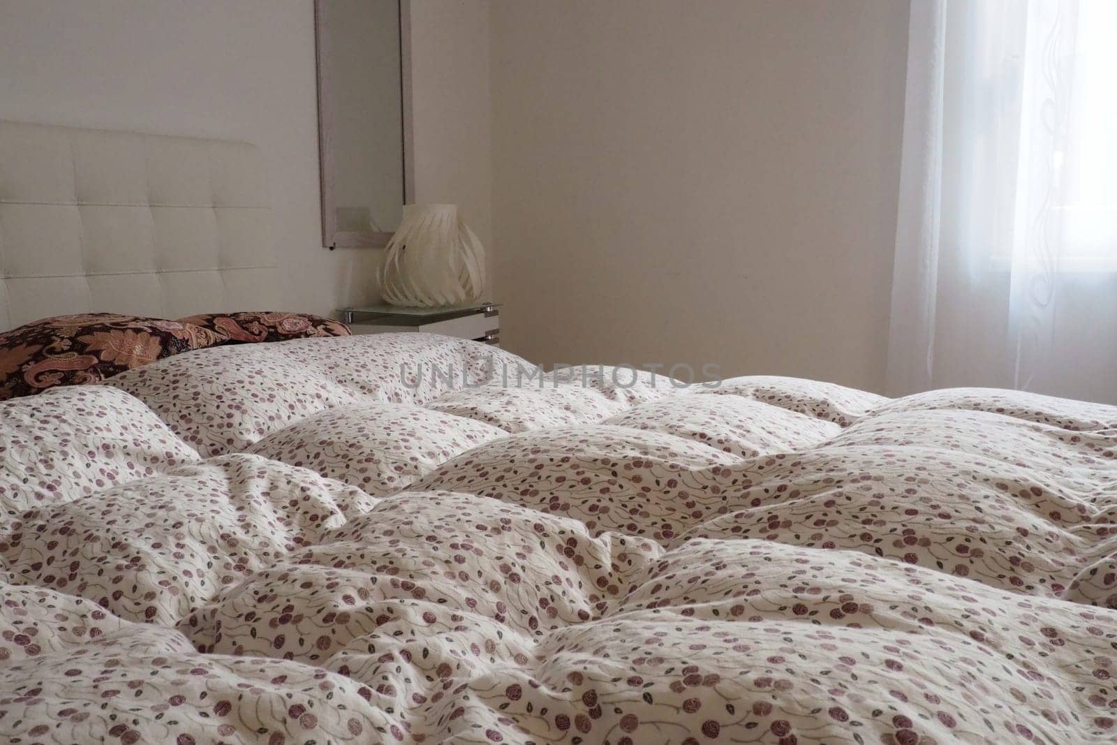 Double bridal bed with pillows and thick feather duvet. Bedroom design. Soft white headboard. Interior with furniture and bedding