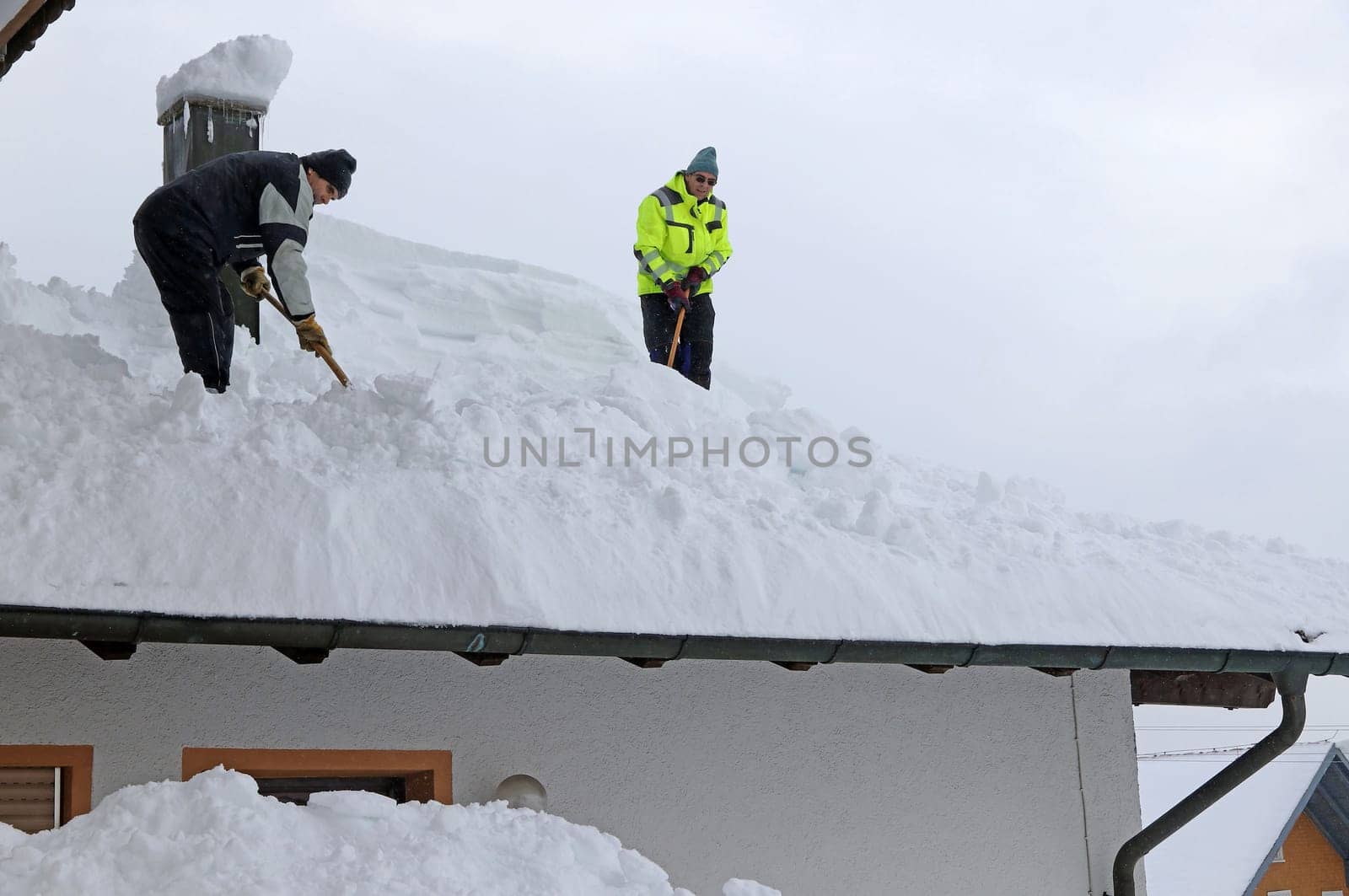 Two men shoveling high heavy snow from a house roof