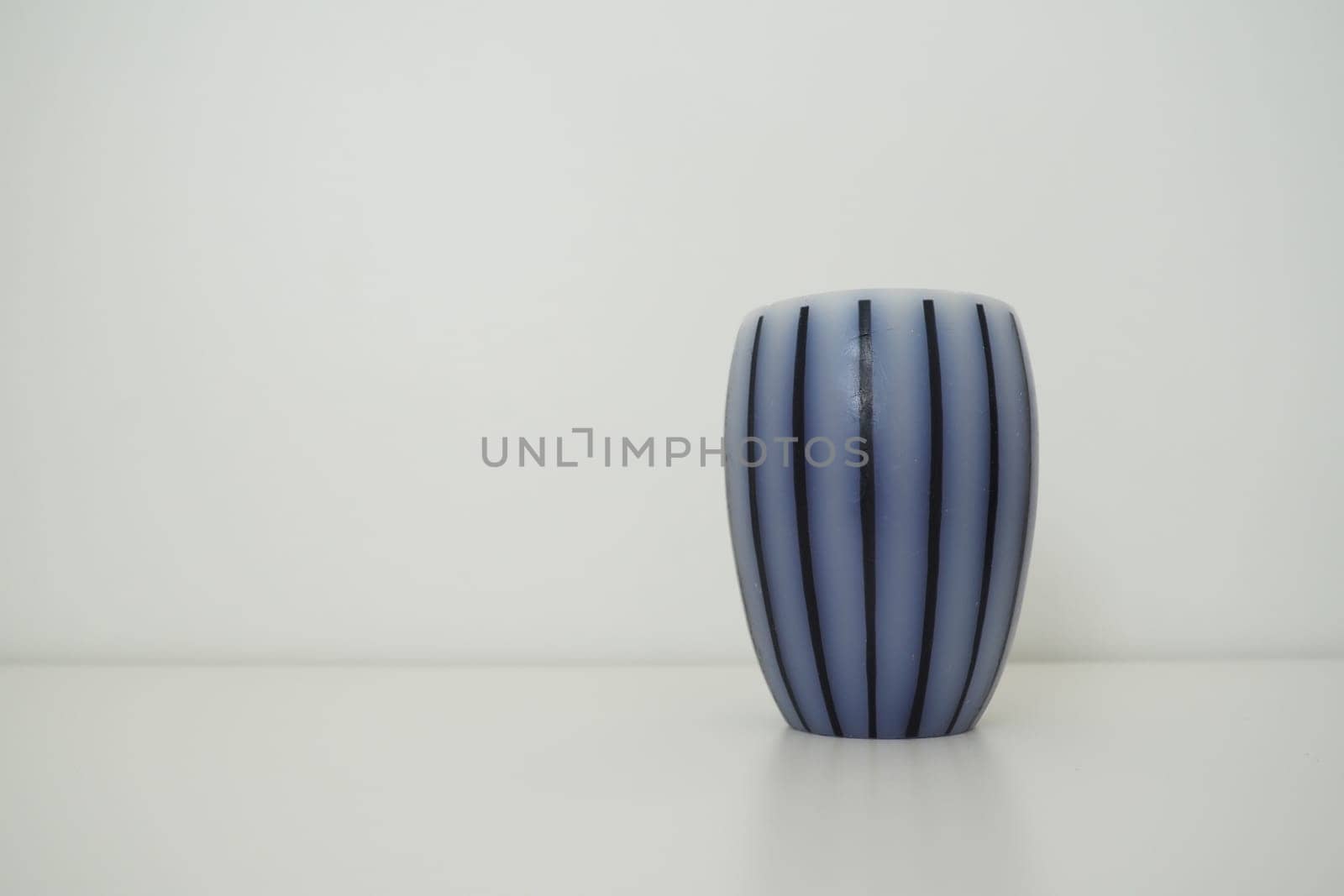 Scented candle on a white surface with a white background behind. Gray striped candle or vase