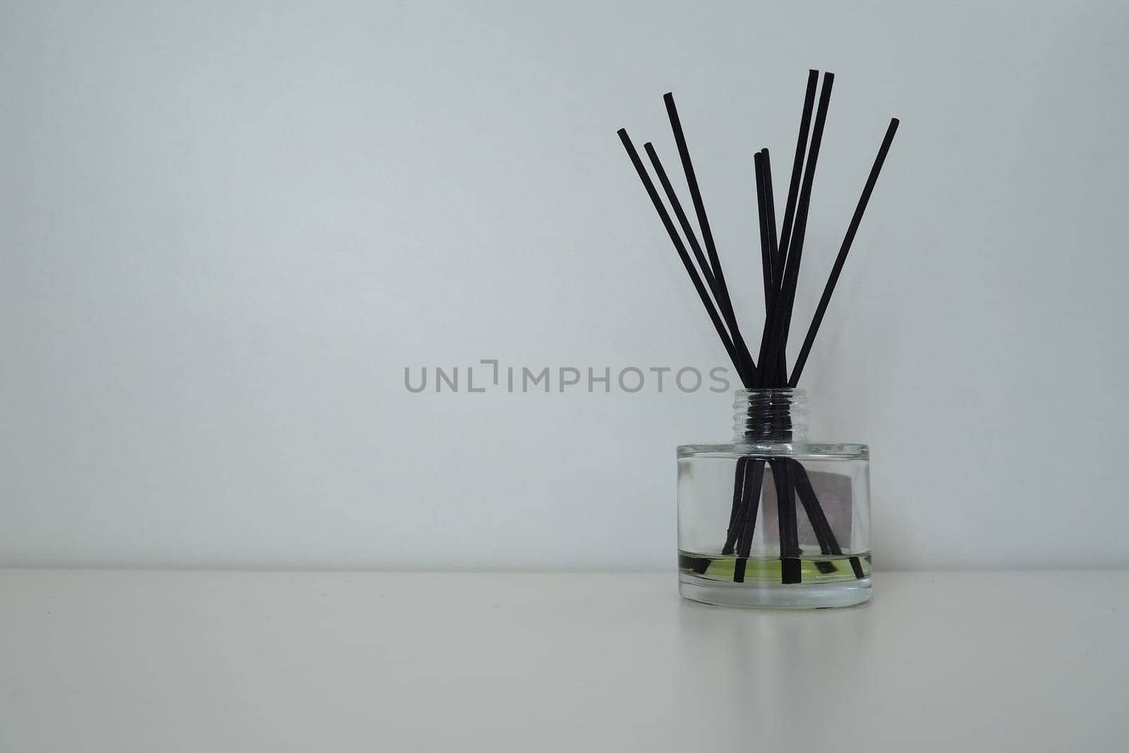Incense sticks are lowered into a glass cubic vessel with essential oils. Interior decor. White background. Still life with sticks to create a pleasant smell in the room