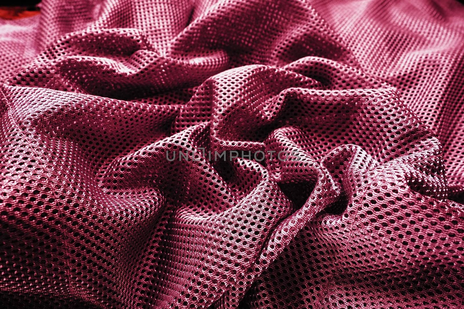 Synthetic fabric with holes, laid in waves and twisted into folds. Beautiful drape. Fabric for curtains, interior design, and decor. Twisted or wrinkled red burgundy porous fabric.
