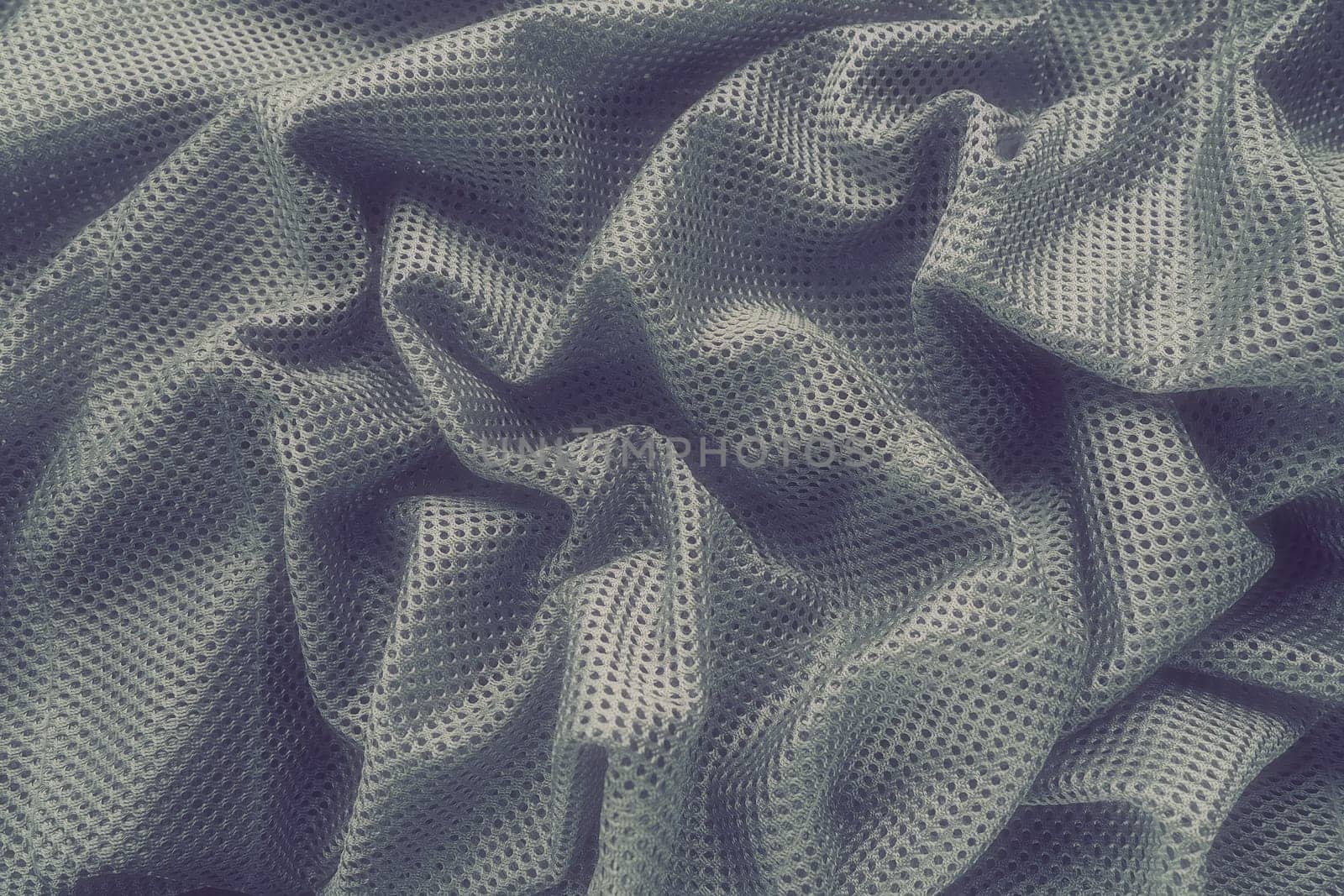 Synthetic fabric with holes laid in waves. Beautiful drape. Fabric for curtains, interior design, and decor. Wrinkled gray fabric
