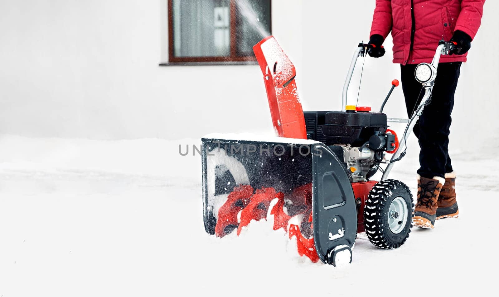 Snow blower powered by gasoline in action. Man outdoor in front of house using snowblower machine. Snow removal, thrower assistant in winter outside home. Young worker guy blowing snow during blizzard
