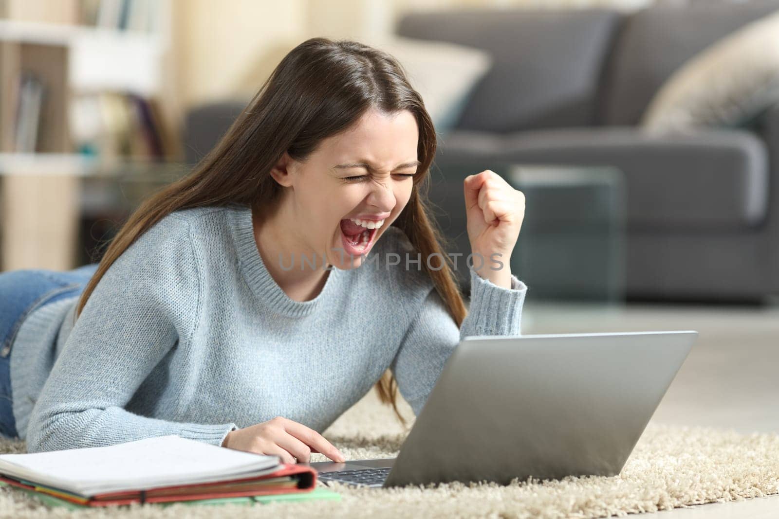 Excited student lying on the floor checking laptop at home