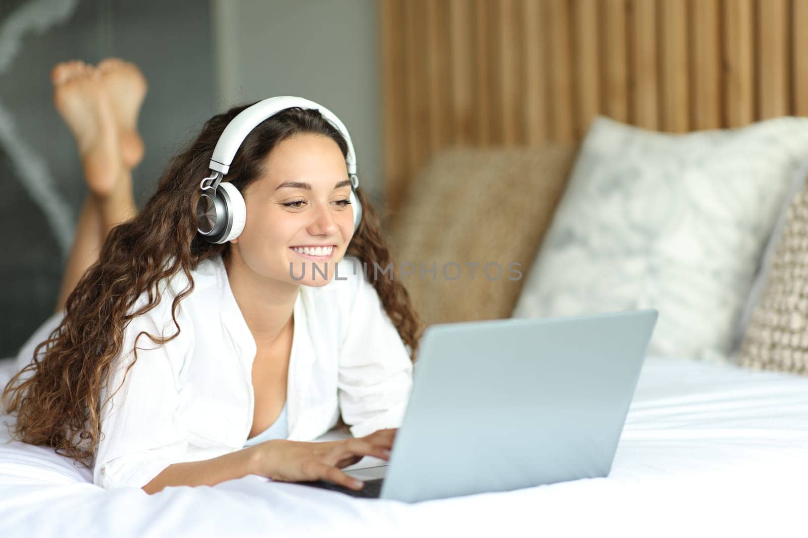 Woman with headphones checking laptop on a bed in the bedroom