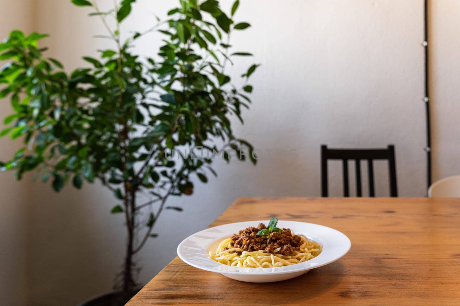 Spaghetti bolognese in a white plate on a wooden table. A classic dish of Italian cuisine.