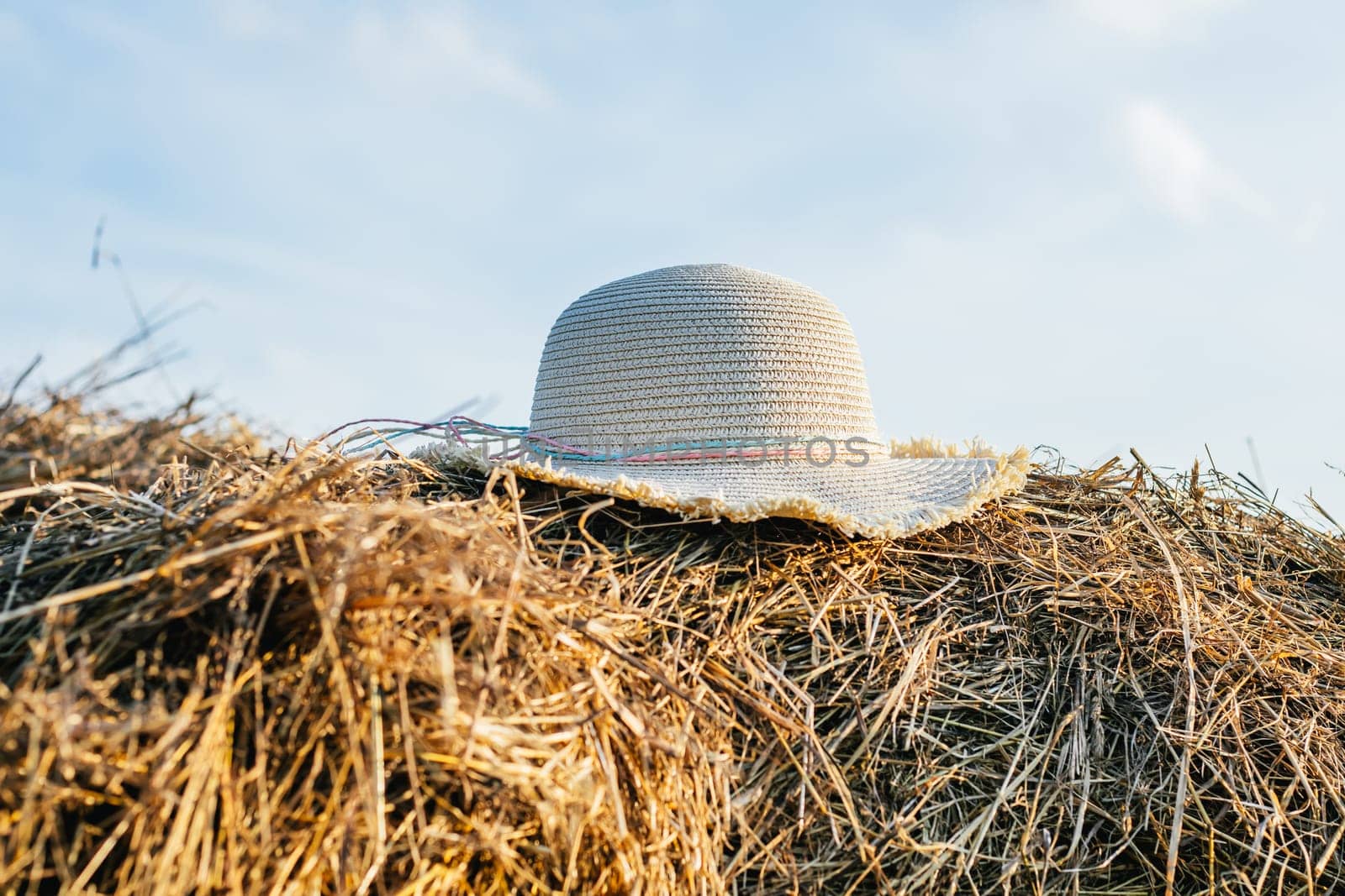 Wicker female panama hat lying at top of haystack. Beautiful clear blue sky. Pile of dry grass. Summer time, countryside lifestyle, haying. Casual clothing, headwear, overheat and sun protection.