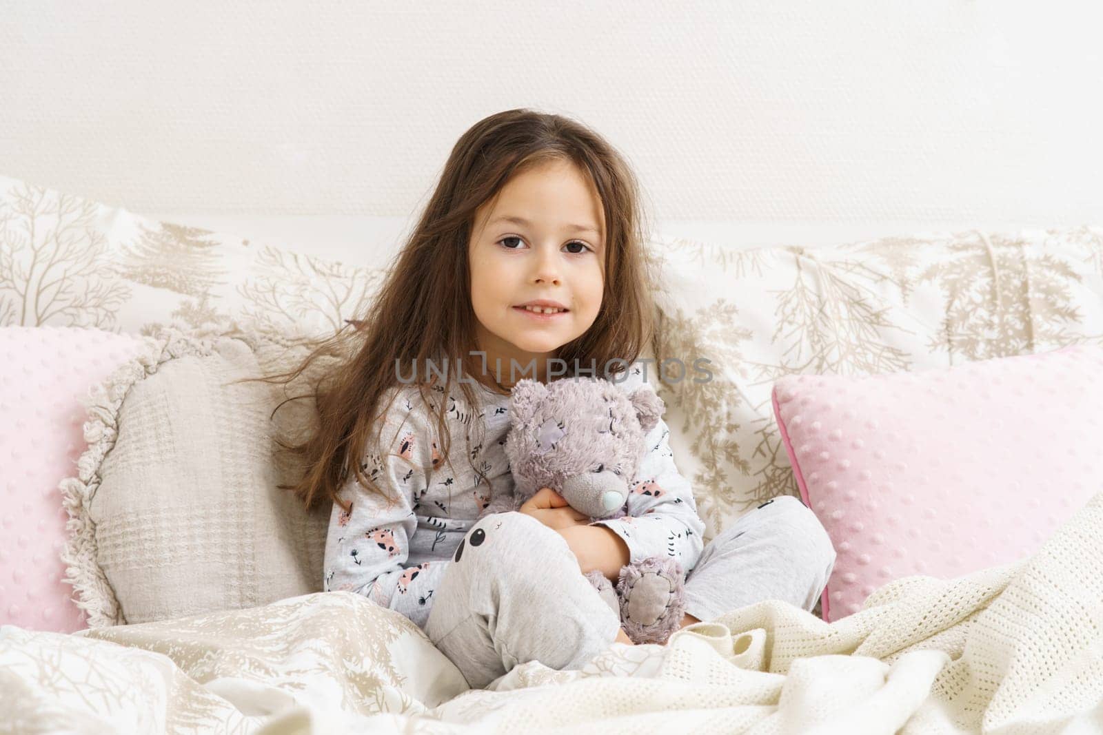 Little girl smiling with sleepy eyes and hugging favorite stuffed toy. Portrait of awaking child. Kid wake up at morning. Sleeping with stuffed toy, teddy bear. Resting on cozy bed, awakening.