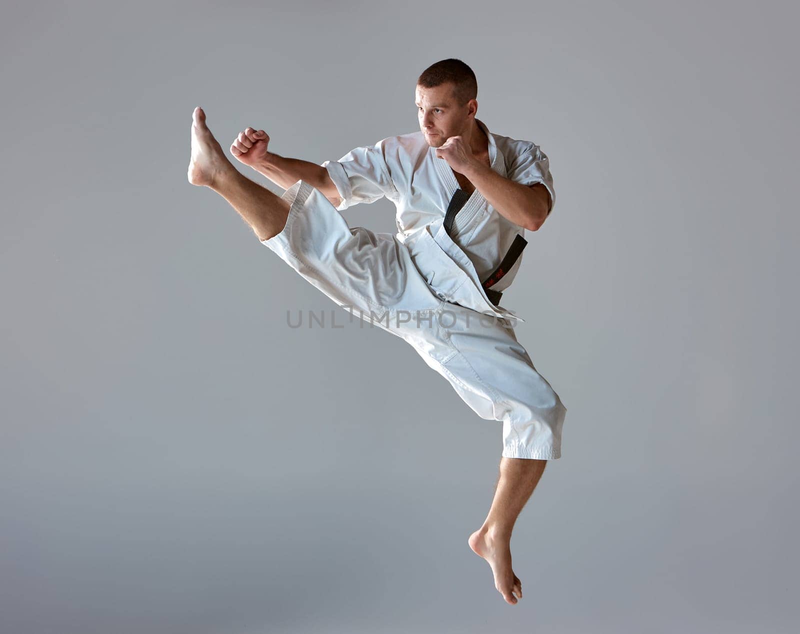 Man in white kimono and black belt training karate over gray background.