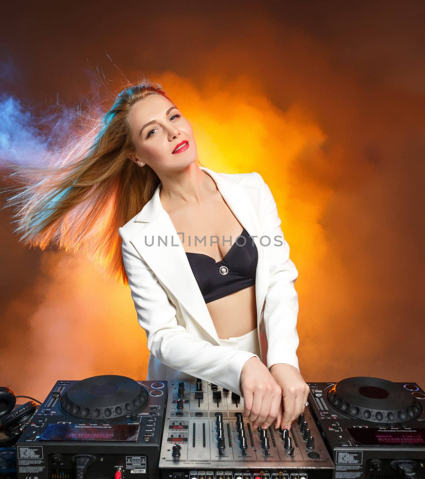 Beautiful blonde DJ girl on decks on the party on the background of orange smoke