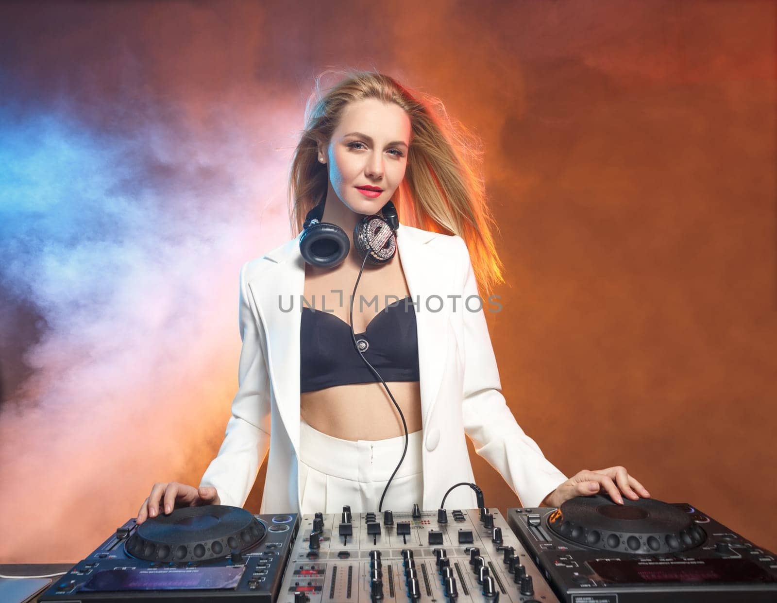 Beautiful blonde DJ girl on decks on the party on the background of orange smoke